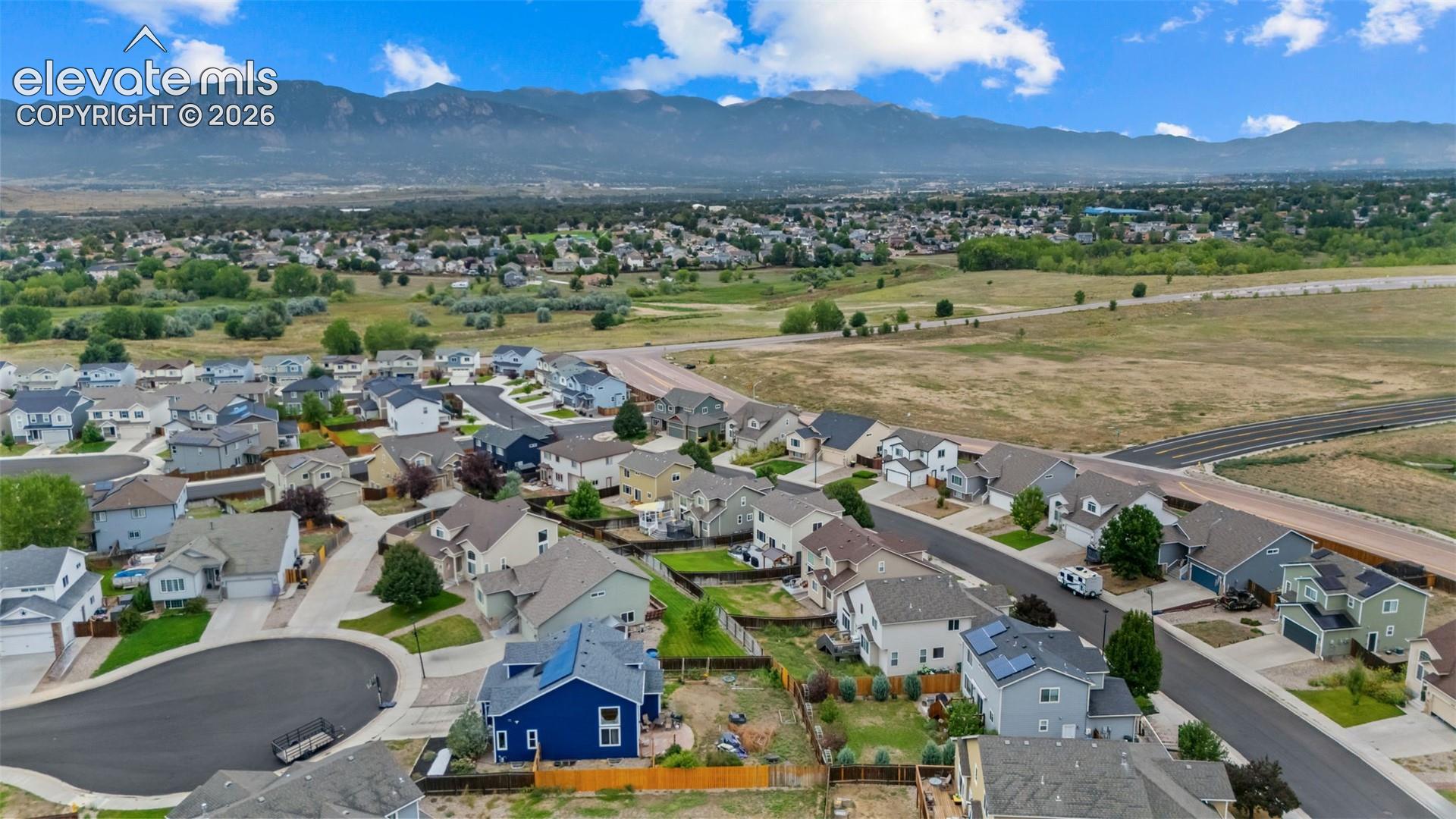 Residential neighborhood with asphalt streets and mature trees, featuring a distant mountain range