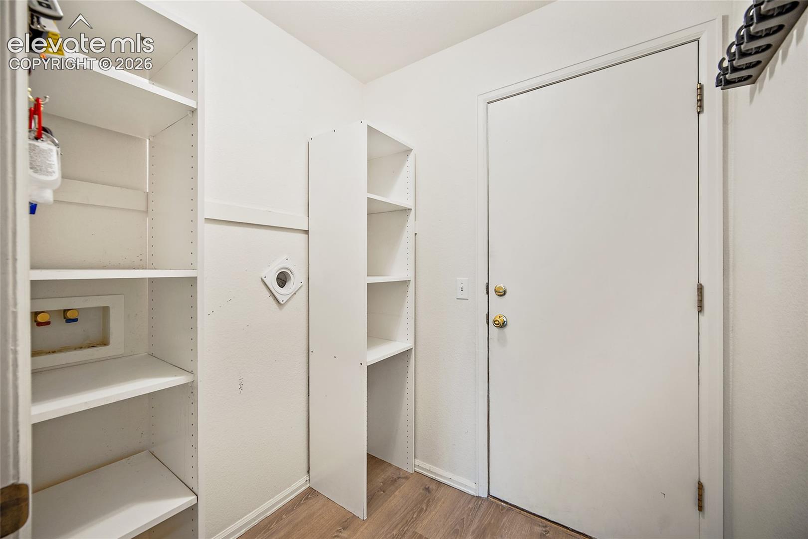 Dedicated utility space featuring built-in shelving, wood-finish flooring, and a white interior door