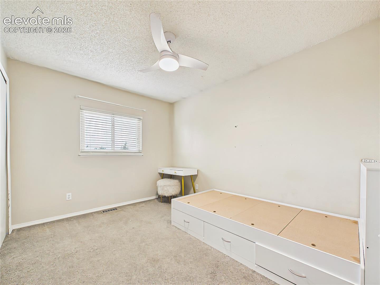 Bright secondary bedroom with plush carpeting, ceiling fan, and a large window providing natural light.