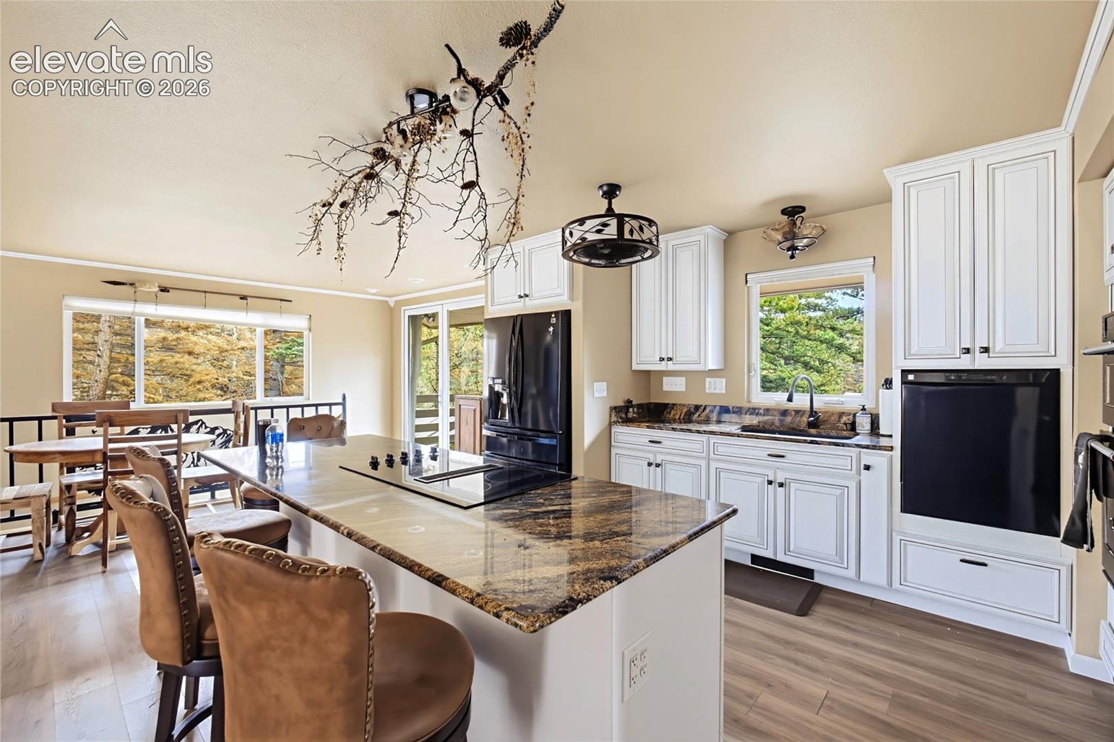 Kitchen featuring white shaker-style cabinetry, stone-surface countertops, central island with an integrated cooktop, wood-finish flooring, and black built-in appliances