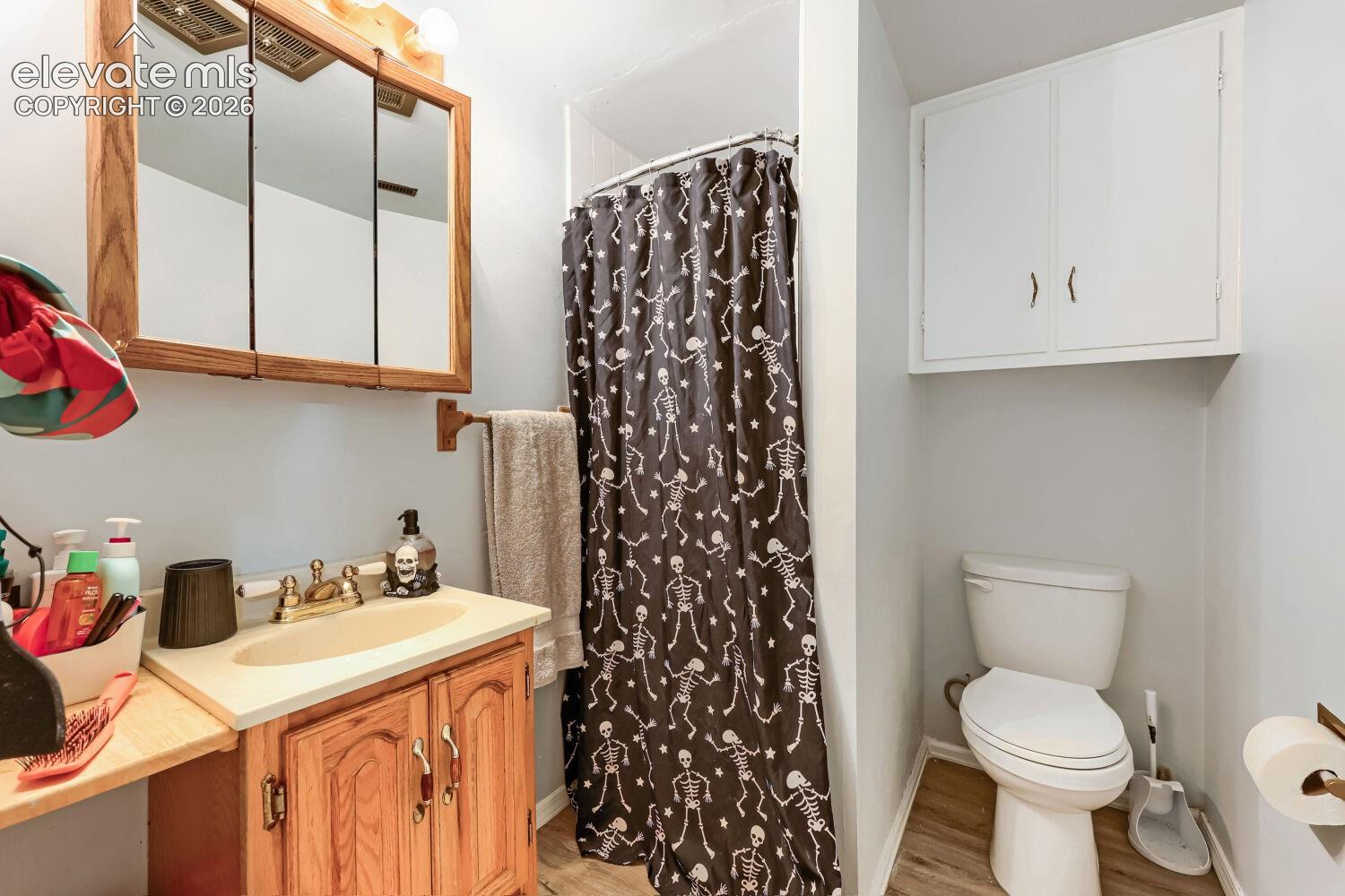 Wood-finish vanity with a built-in sink, wall-mounted medicine cabinet, white wall cabinetry, and wood-finish flooring