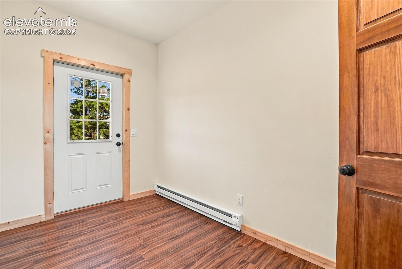 Wood-finish flooring, six-panel solid wood interior door, and white exterior door featuring a nine-pane glass insert with natural wood trim