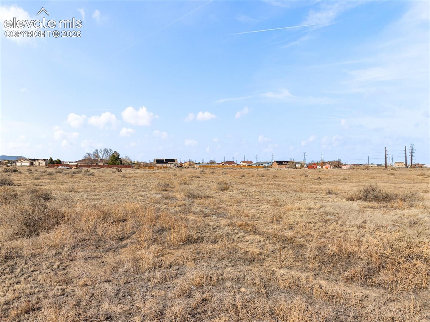 Expansive undeveloped land with distant residential structures and utility poles