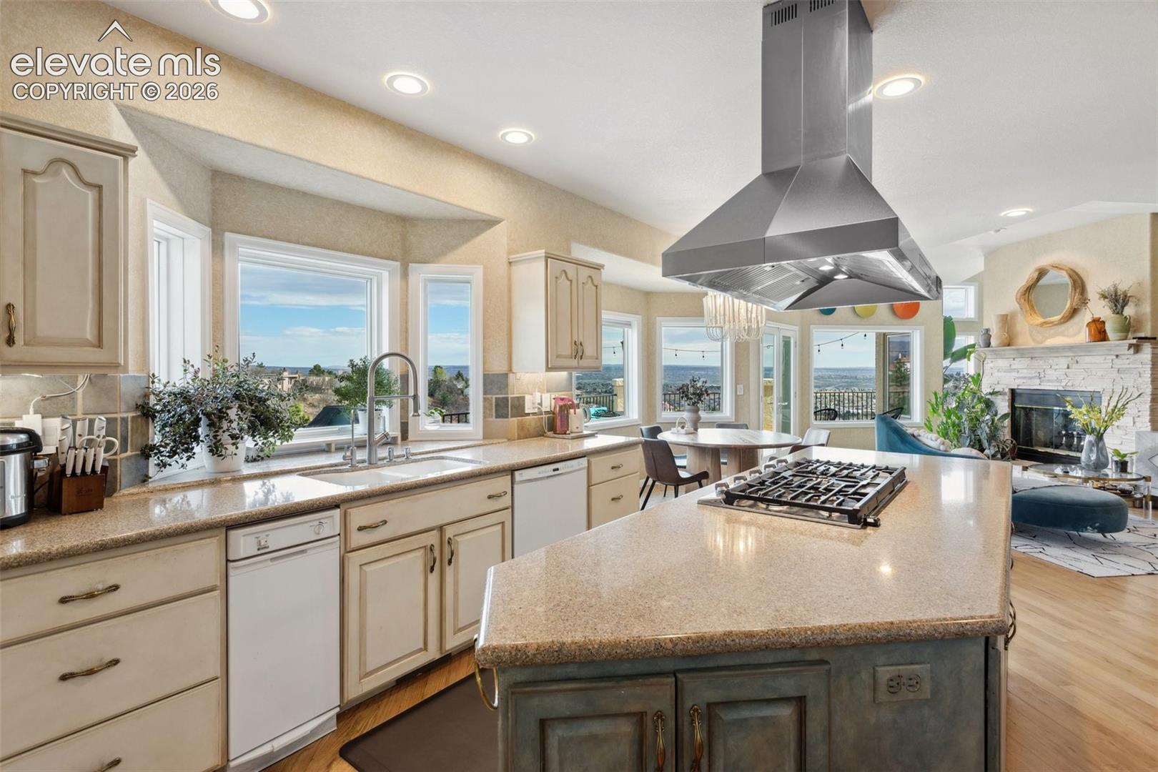 Kitchen featuring an island with a built-in gas cooktop, stainless steel range hood, bay window over the sink, recessed lighting, and hardwood flooring