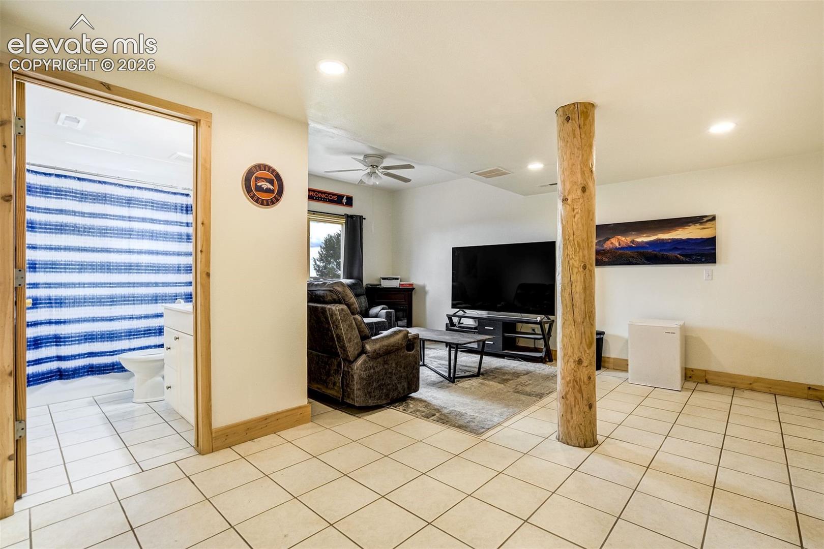 Open concept living area with tiled flooring, featuring a natural wood support column, recessed lighting, and a visible bathroom with a white vanity and toilet