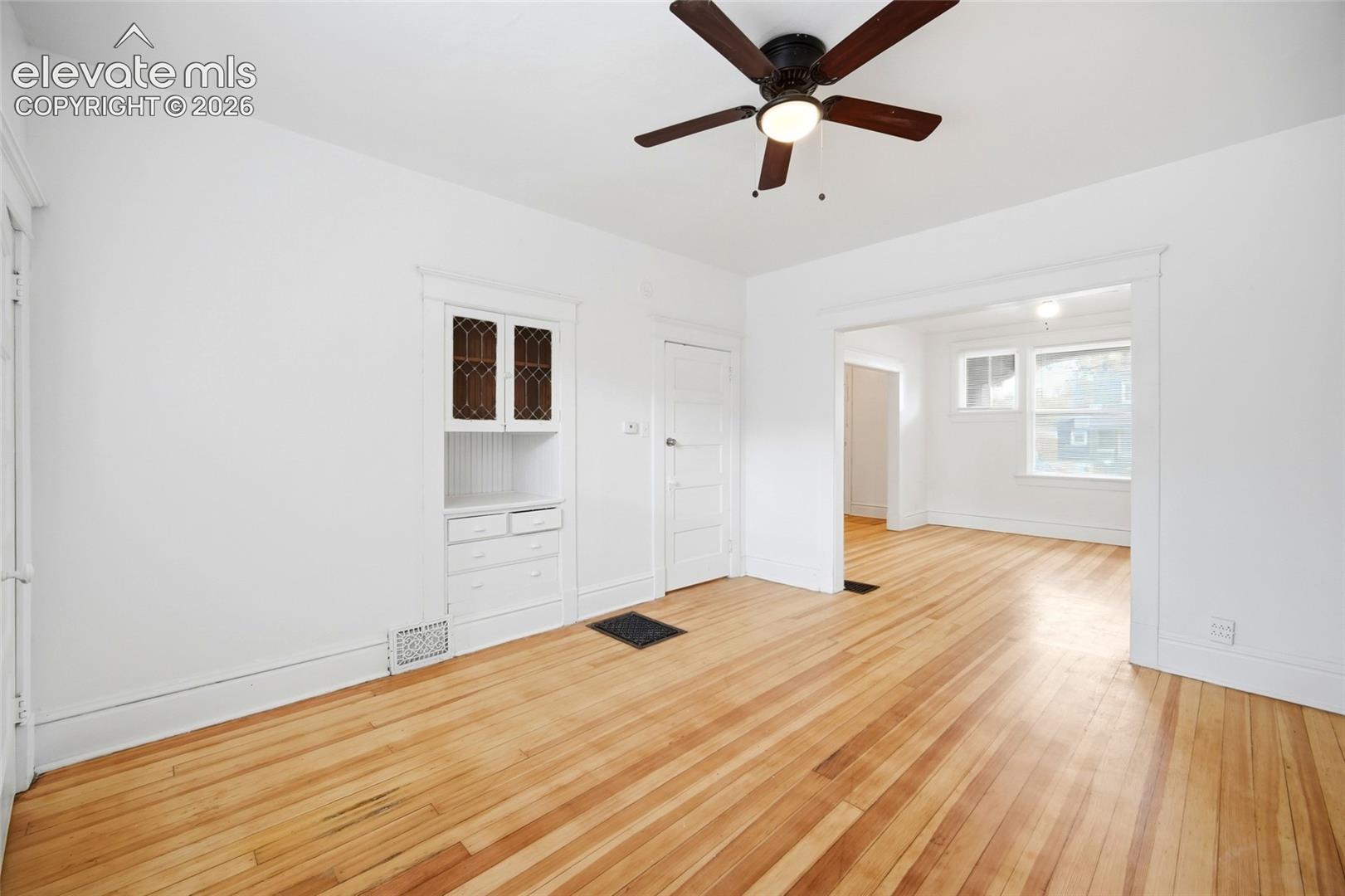 Wood-finish flooring, built-in cabinetry featuring leaded glass detailing, and a ceiling-mounted light fixture with a fan