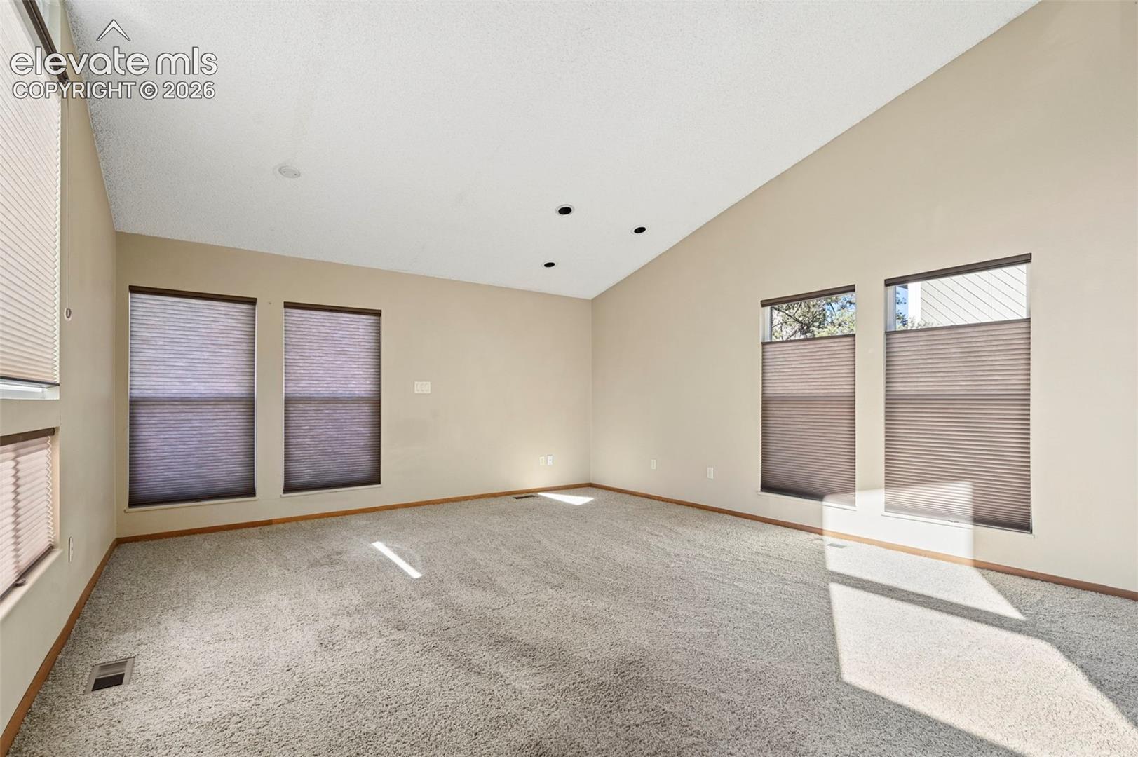 Vaulted ceilings, neutral wall tones, recessed lighting, and expansive windows featuring pleated shades