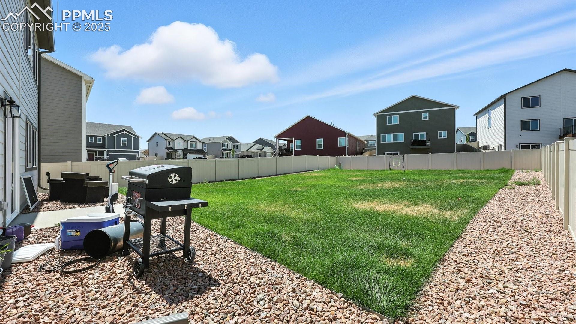 View of the fenced backyard with xeriscaped rock gardens and green grass.