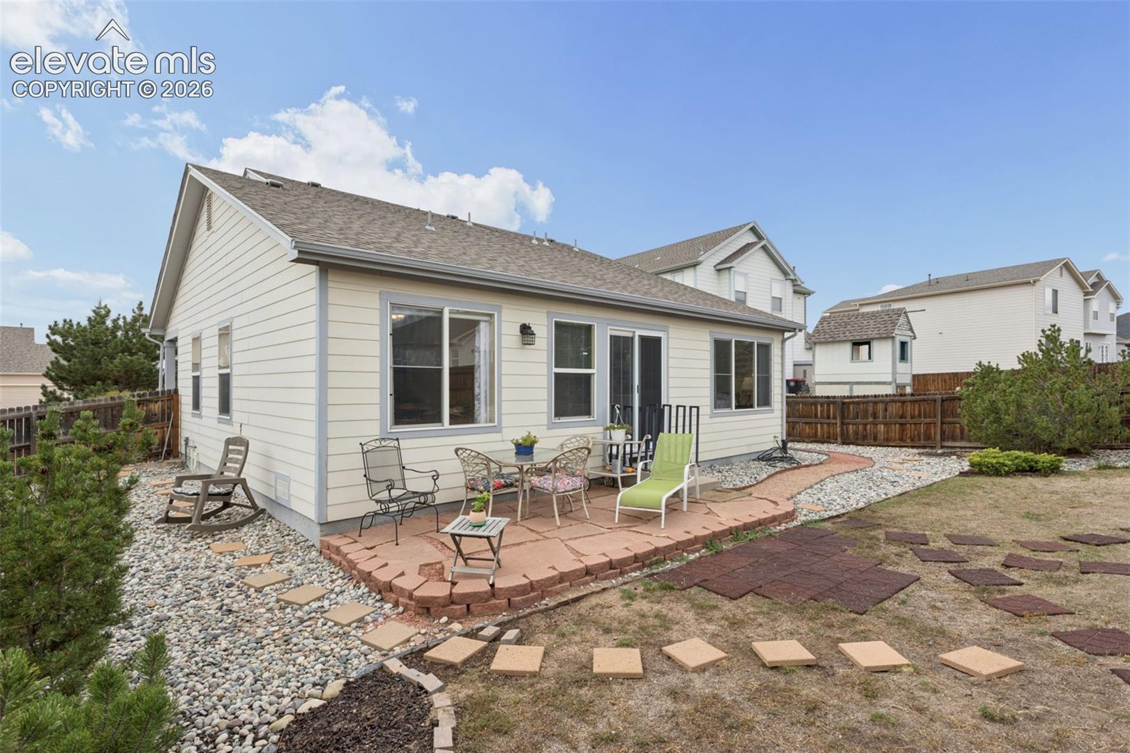 Rear exterior featuring a flagstone patio, sliding glass door, multiple windows, and a landscaped rock border