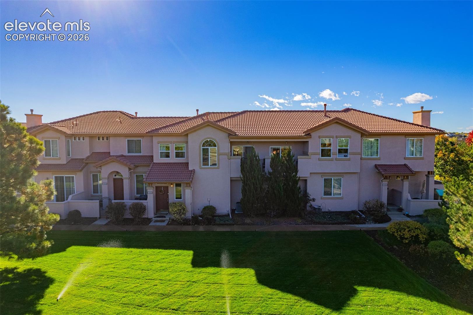 Multi-level stucco exterior featuring a clay tile roof, arched entryway accents, second-story balconies, and a manicured lawn