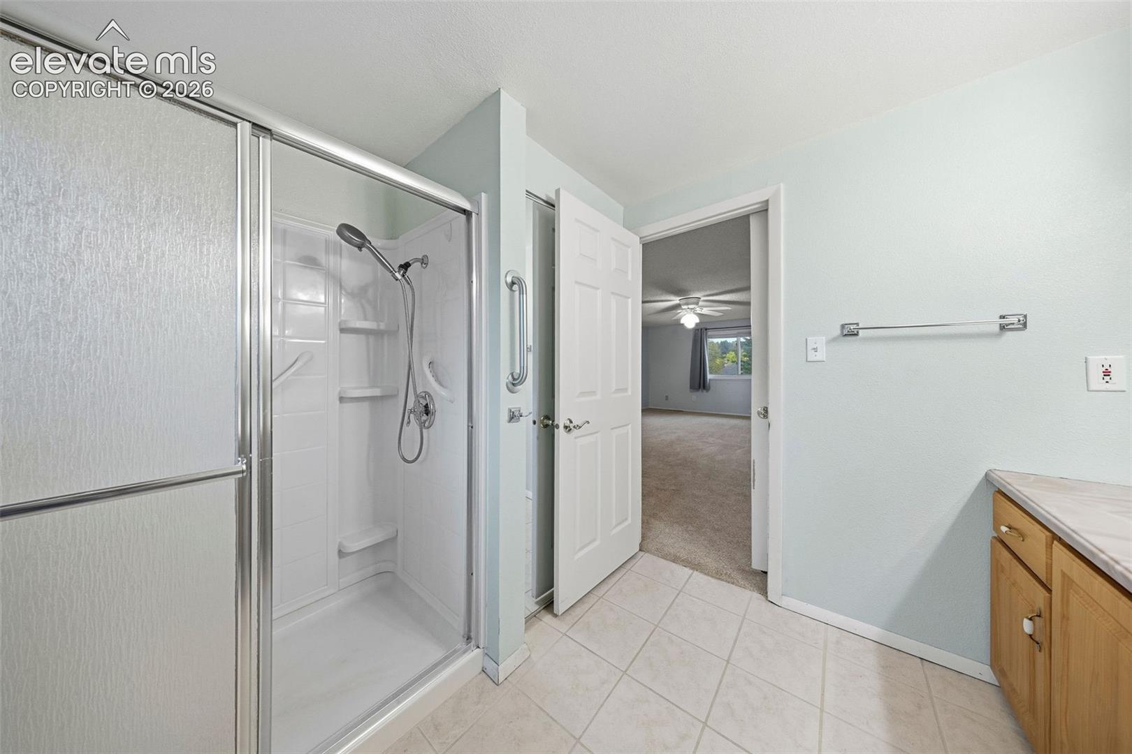 Bathroom featuring a walk-in shower with glass enclosure, integrated shelving, and a handheld showerhead, complemented by tile flooring, wooden cabinetry, and a mounted towel bar