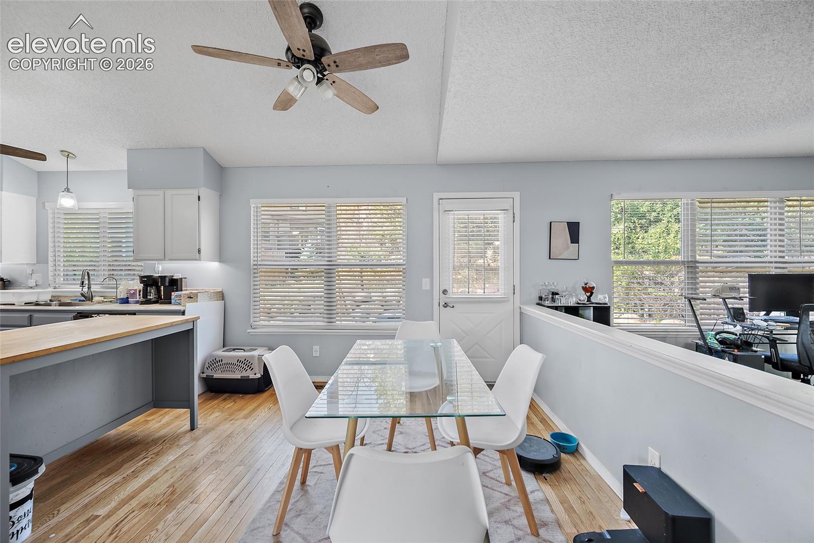 Vaulted ceiling with a ceiling fan, hardwood-finish flooring, white cabinetry, and multiple windows