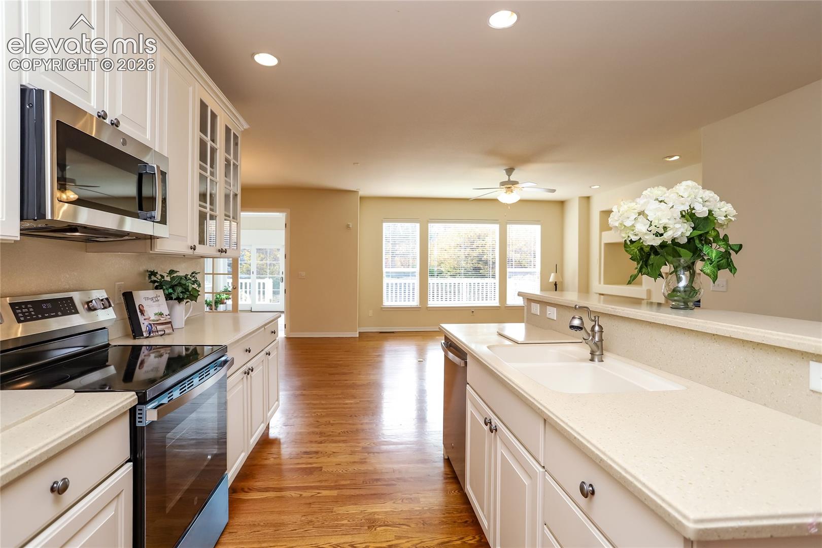 Kitchen featuring white cabinetry with glass-panel accents, solid-surface countertops, integrated stainless steel appliances, and wood-finish flooring