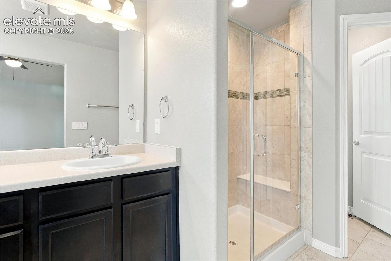 Bathroom featuring dark-finish cabinetry, a solid-surface vanity countertop with an integrated basin, a large-format mirror, and a walk-in shower with a glass enclosure and built-in bench