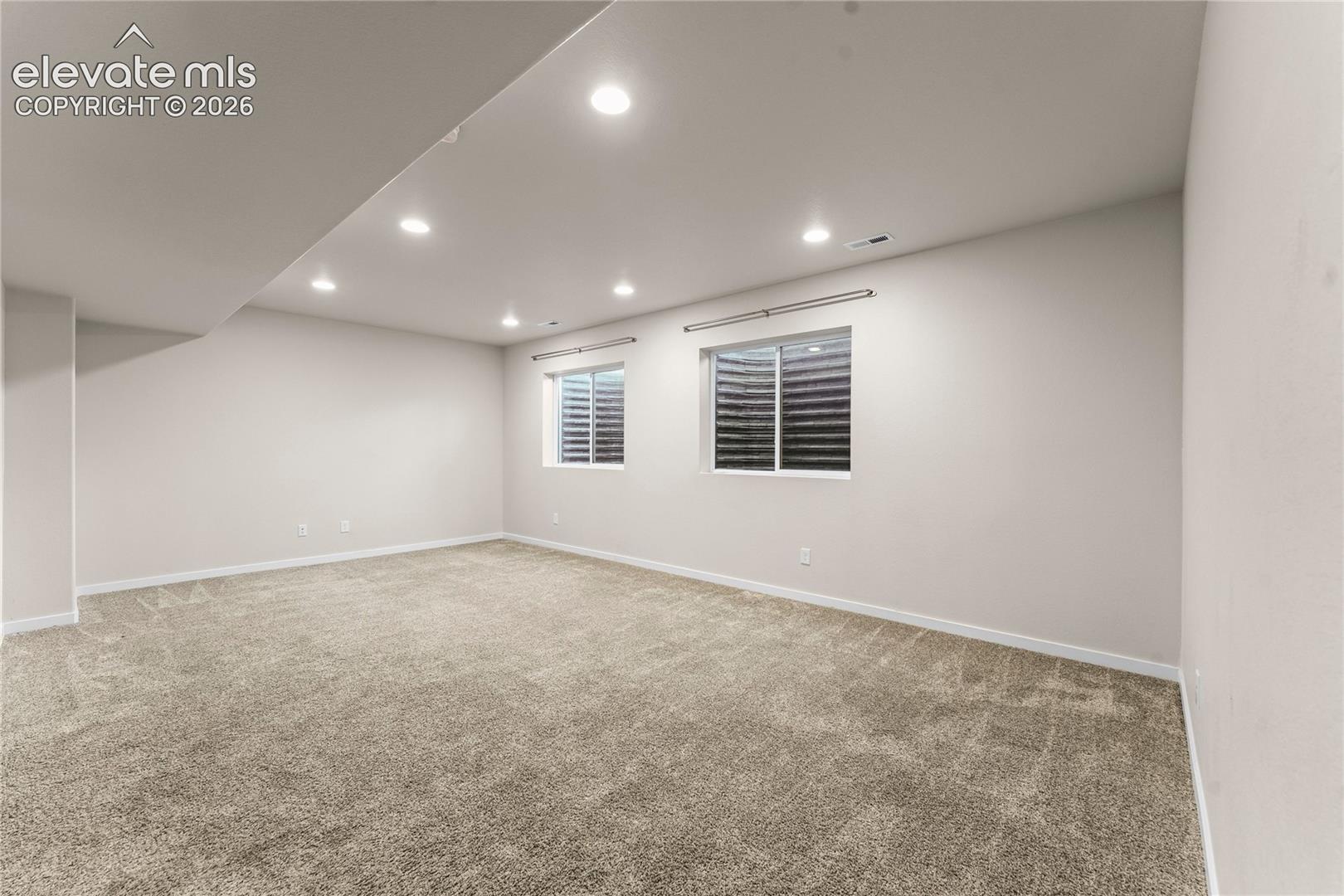 Neutral-toned interior space featuring recessed ceiling lighting, wall-to-wall carpeting, and two egress windows with window wells