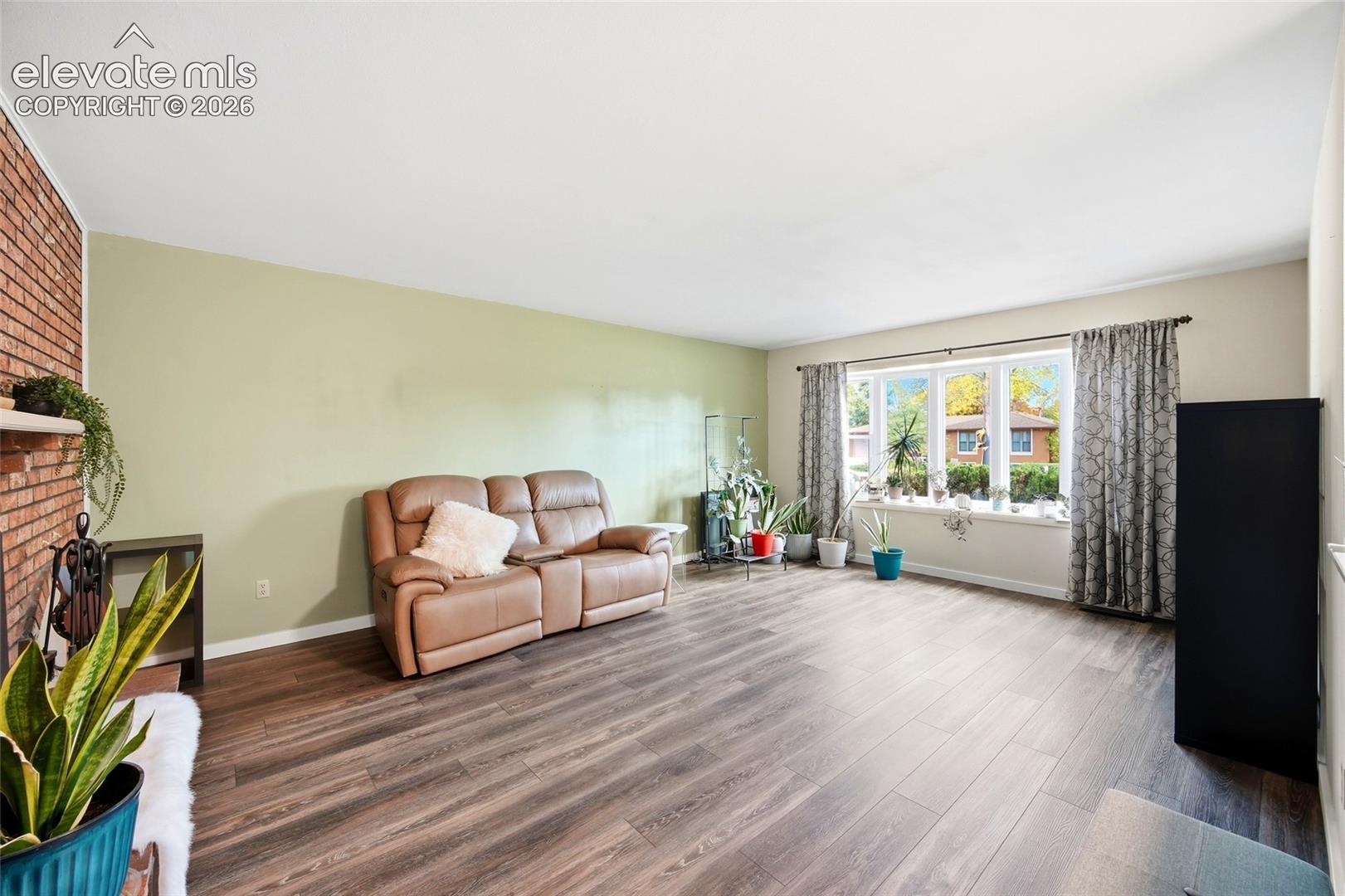 Living area featuring wood-finish flooring, a floor-to-ceiling brick hearth, and a large multi-pane window