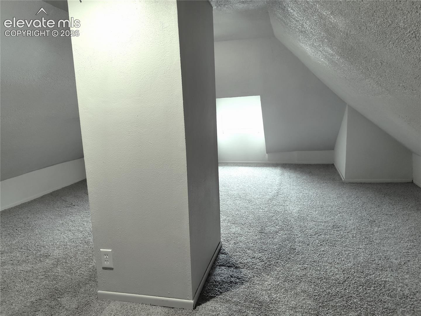 Carpeted flooring with sloped ceilings and a rectangular window