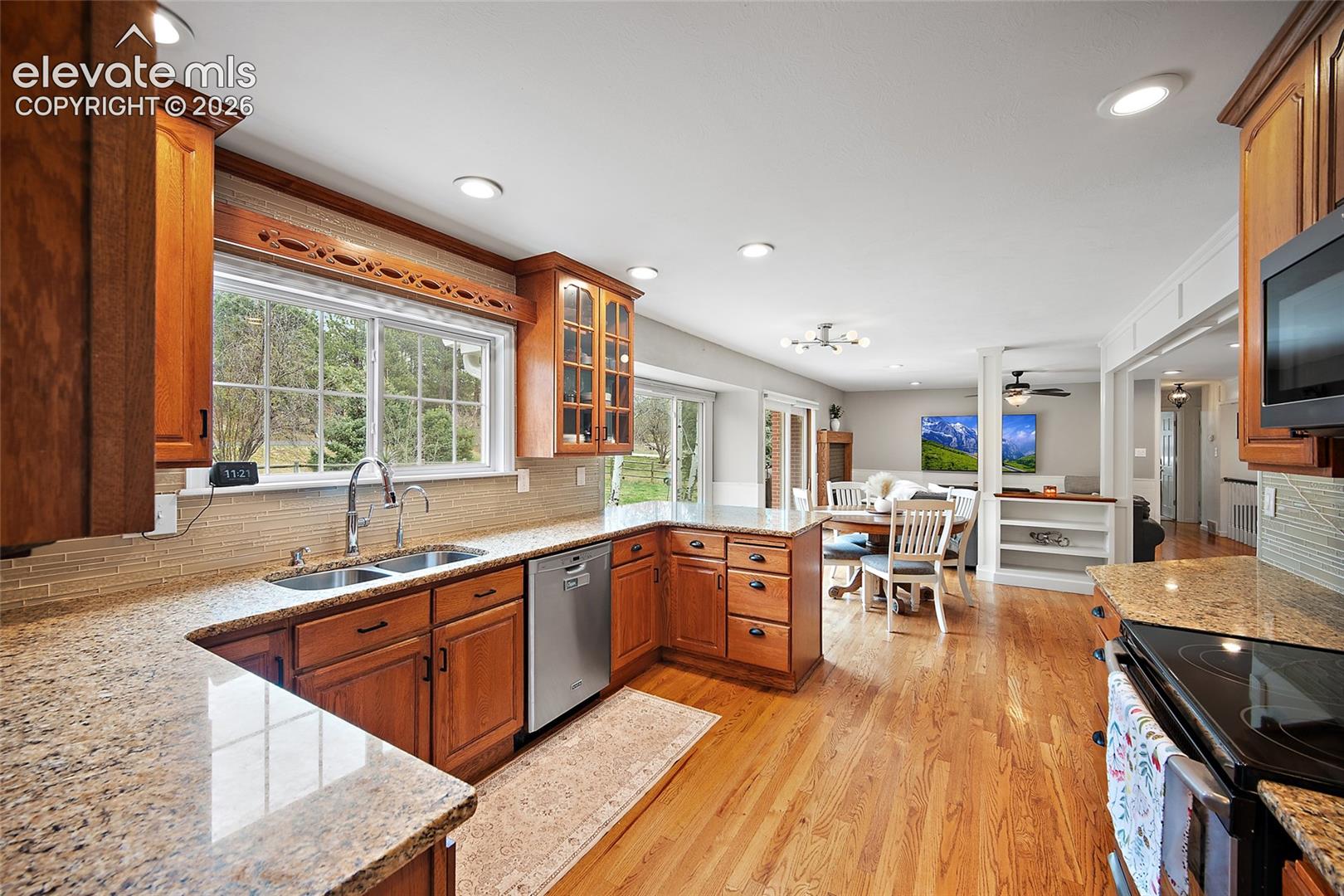 Kitchen featuring custom wood cabinetry, stone countertops, stainless steel appliances, a mosaic tile backsplash, and wood-finish flooring