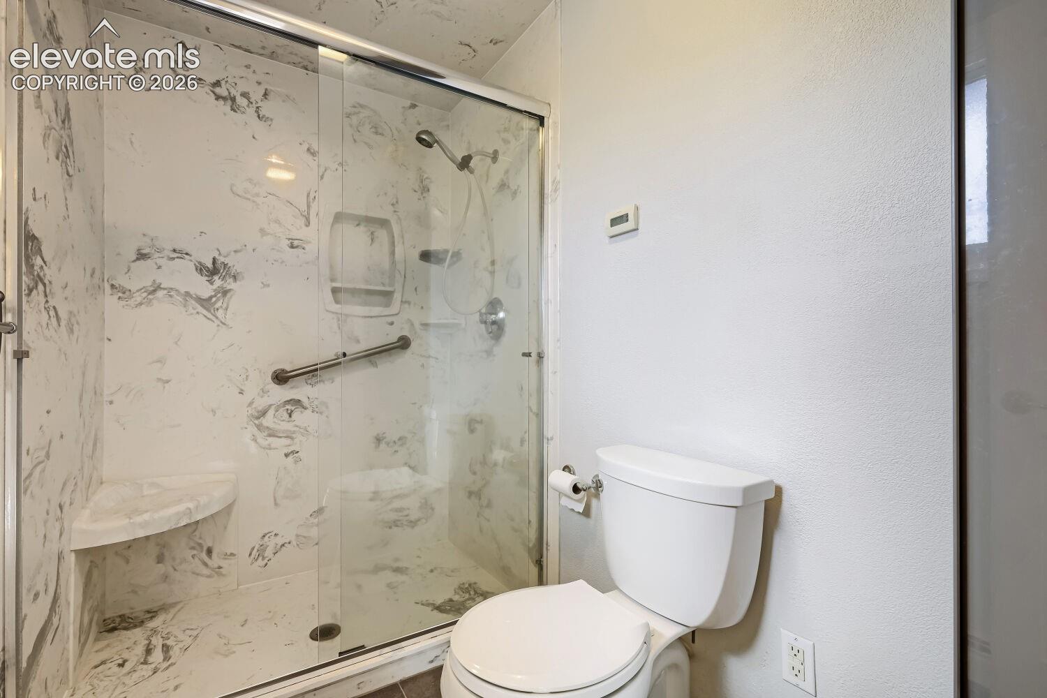 Glass-enclosed shower with marbled surround and integrated bench seating