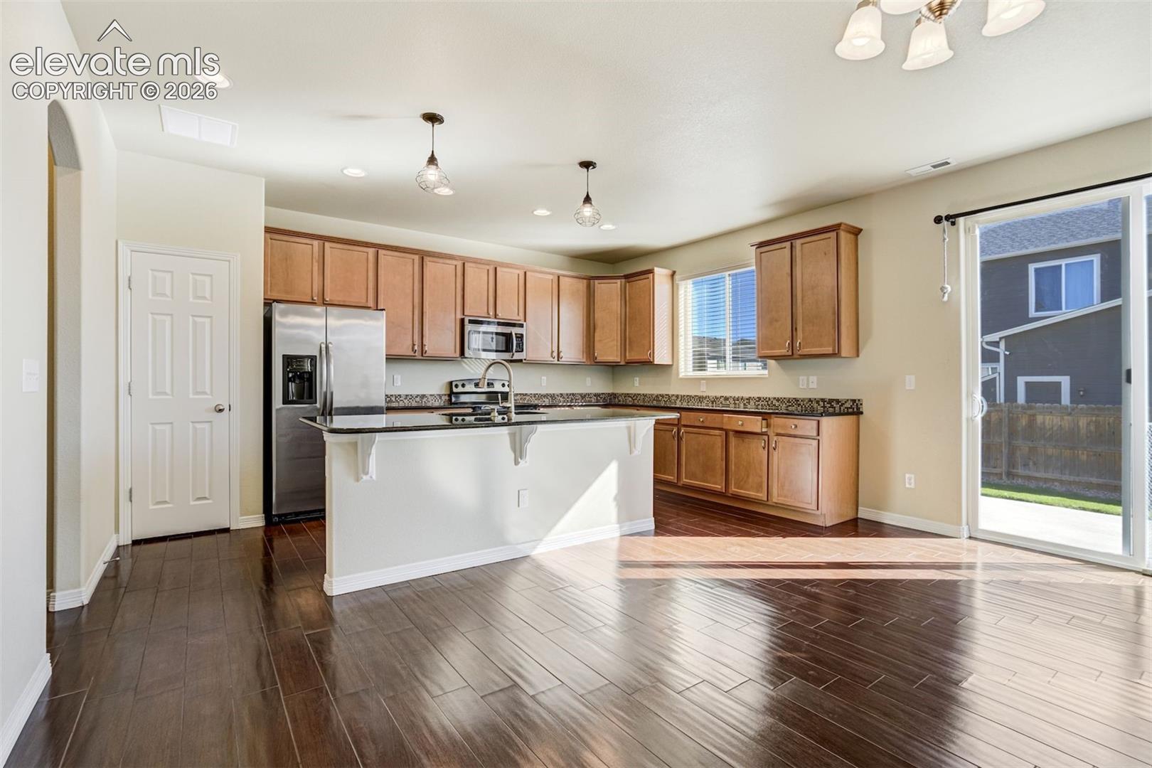 Rich wood-finish flooring, warm wood cabinetry, dark countertops, and stainless steel appliances