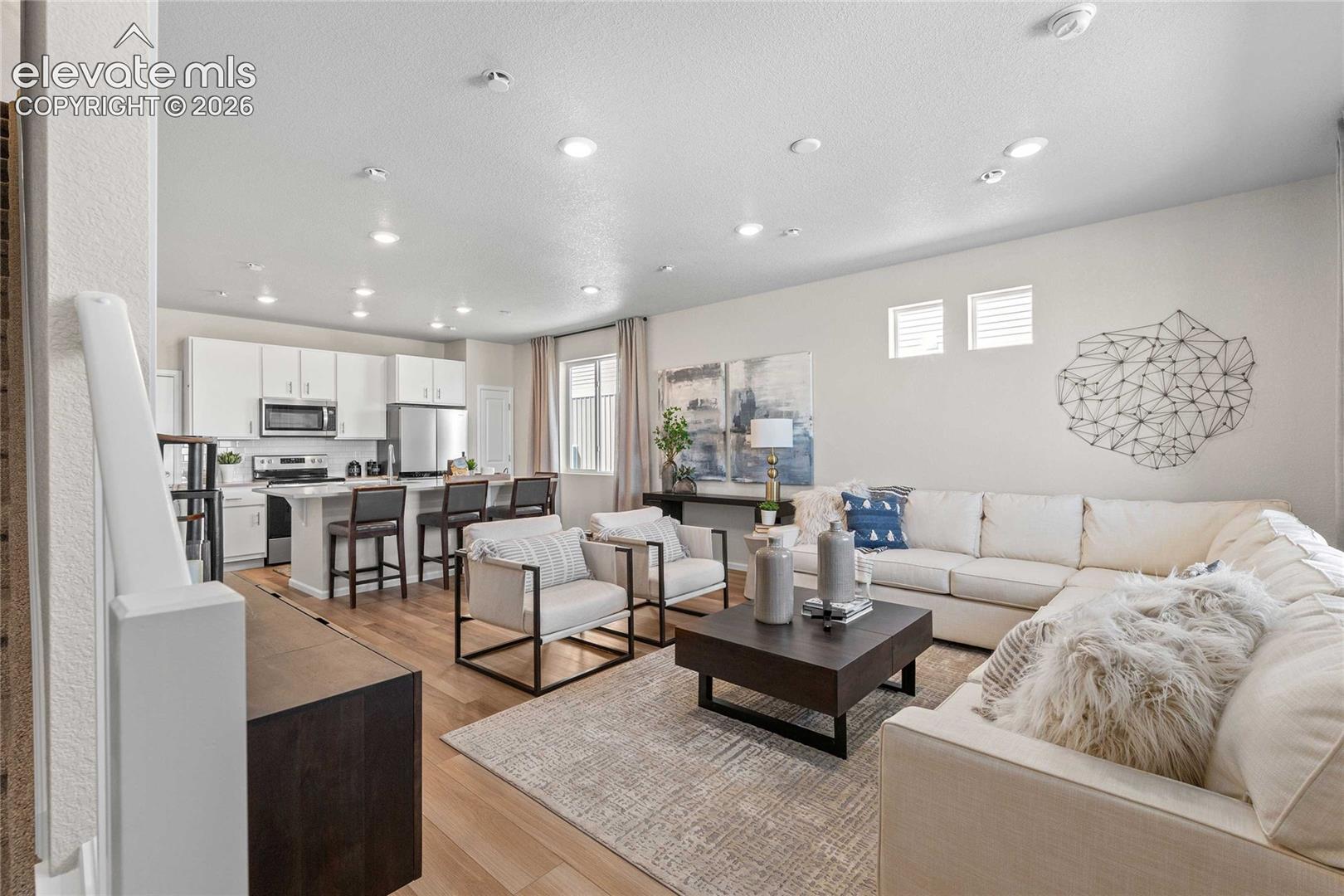 Open-concept living space featuring wood-finish flooring, recessed lighting, and white cabinetry with stainless steel appliances
*photos of a model home*