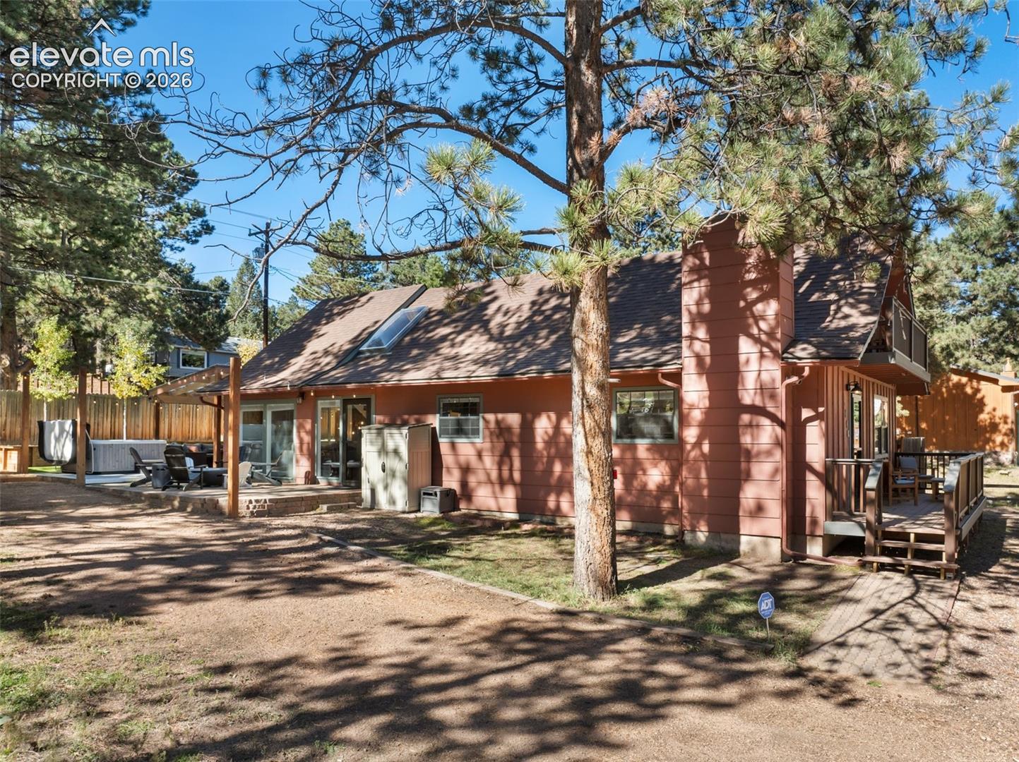 Exterior featuring horizontal siding, a prominent chimney, skylight, a covered stone patio, and an elevated wood deck