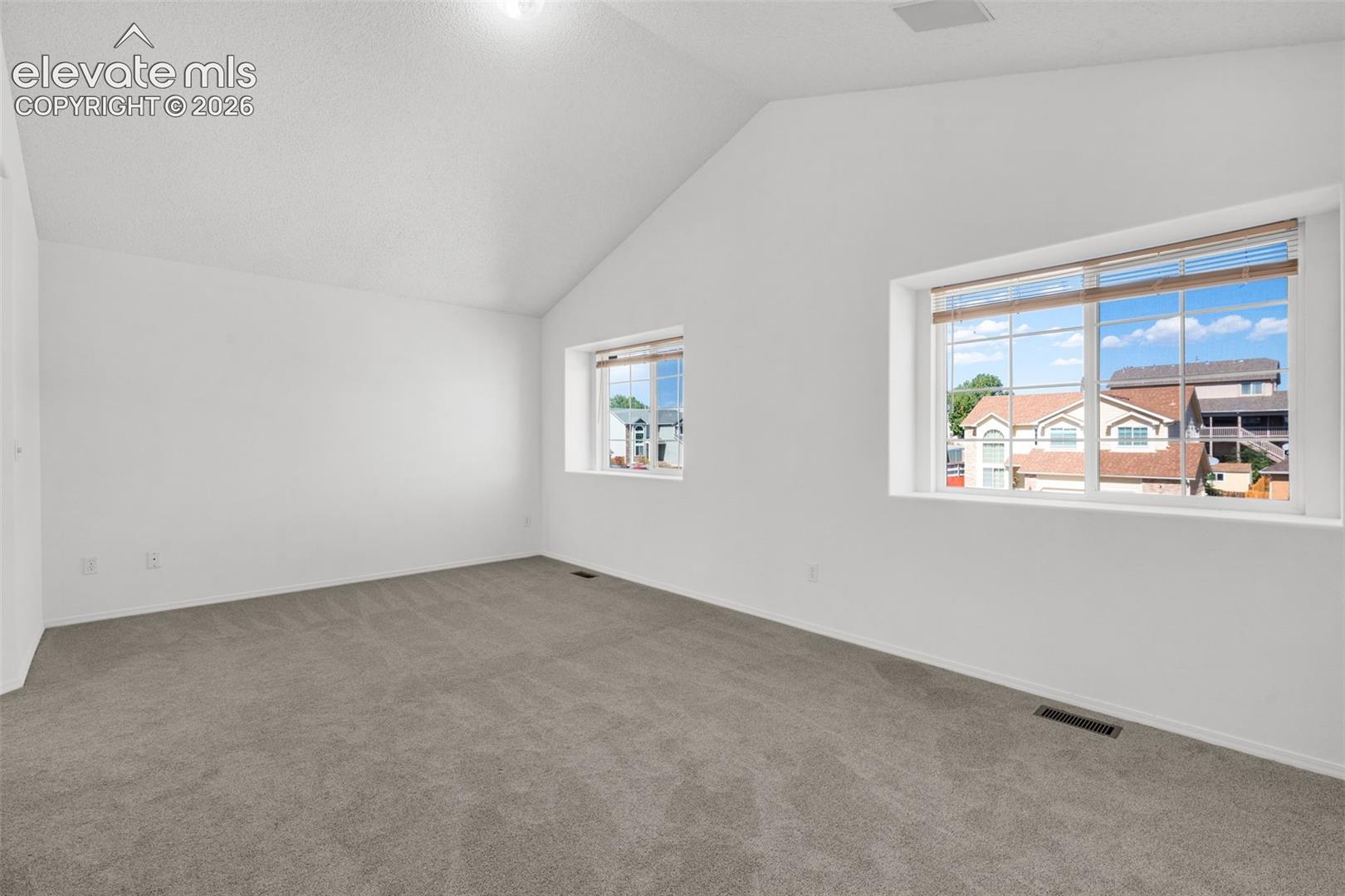 Vaulted ceiling, two windows with blinds, light gray carpet, and white painted walls