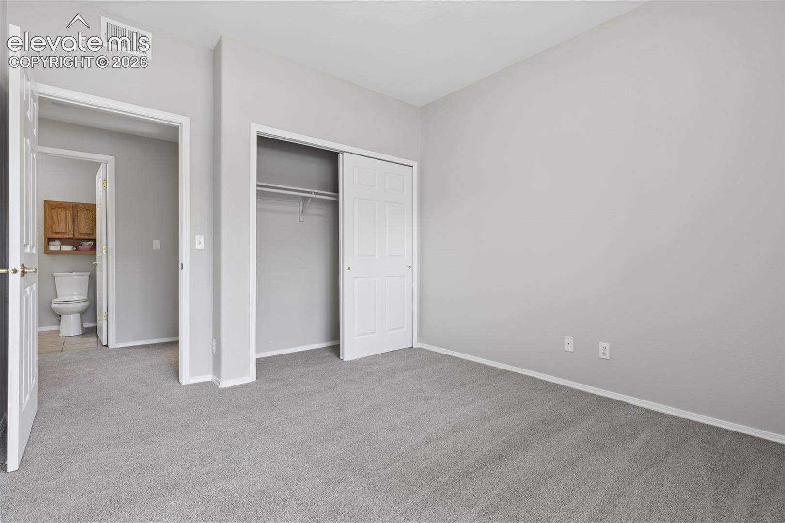 Neutral-toned wall paint, gray carpeting, white trim, and a built-in closet with sliding doors