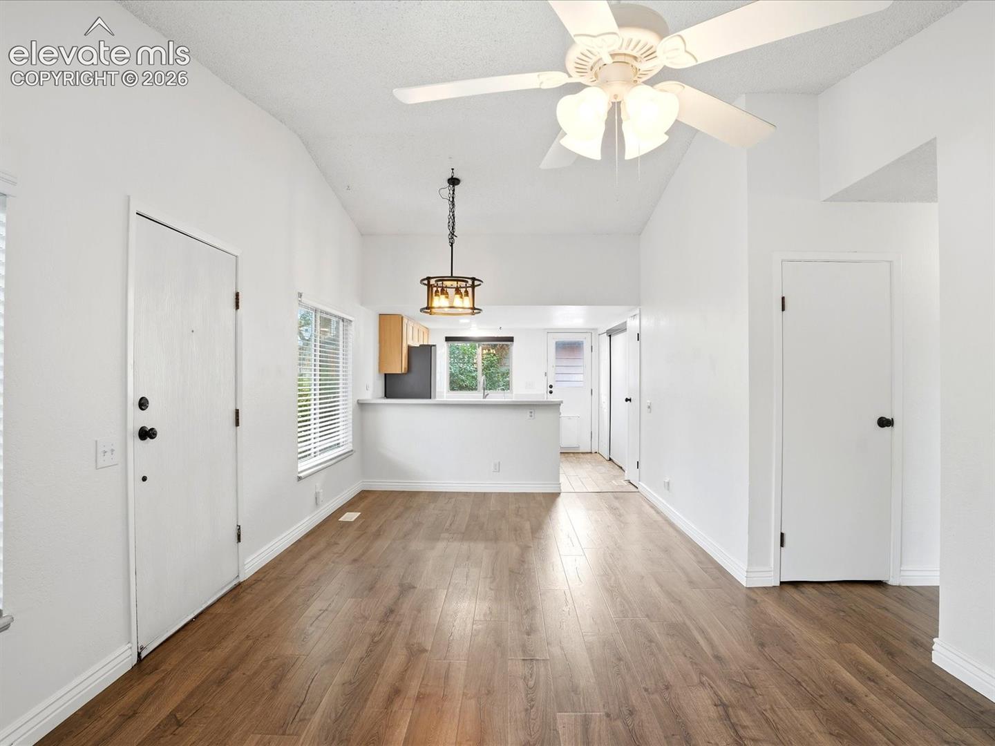 Open floor plan featuring wood-finish flooring, vaulted ceilings, a ceiling fan with integrated lighting, and a pendant light fixture