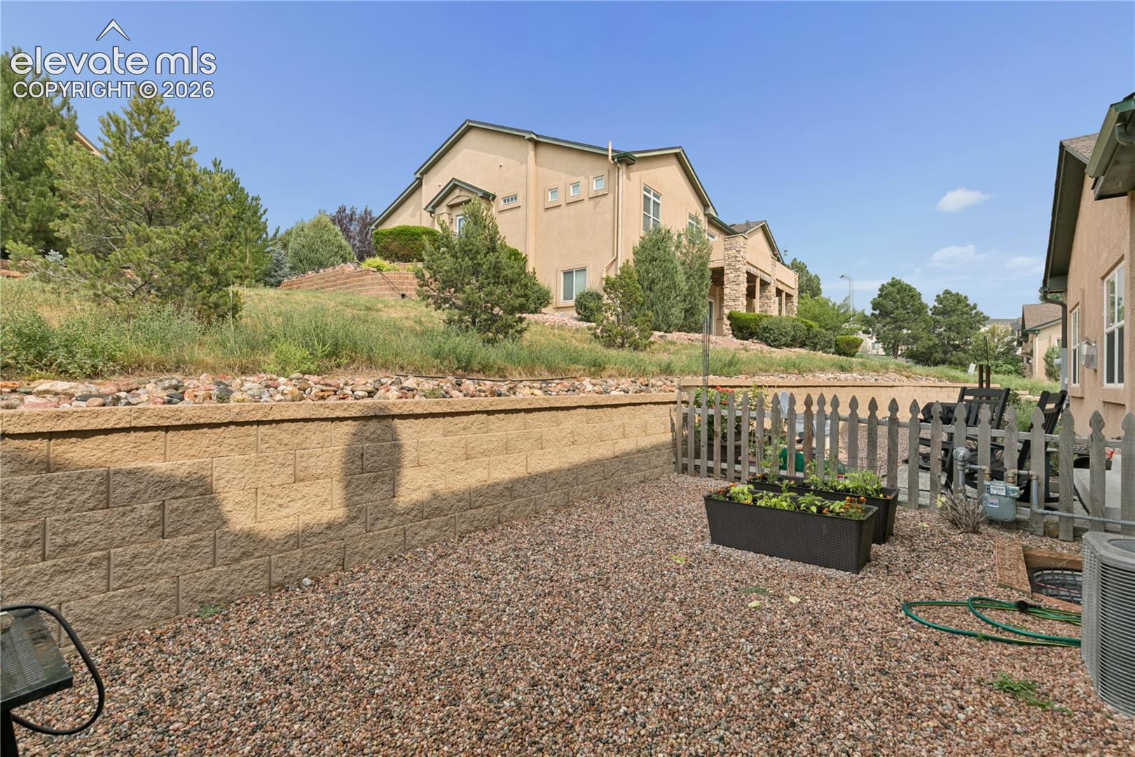 Xeriscaped rear yard featuring a block retaining wall, gravel ground cover, and a picket fence enclosure