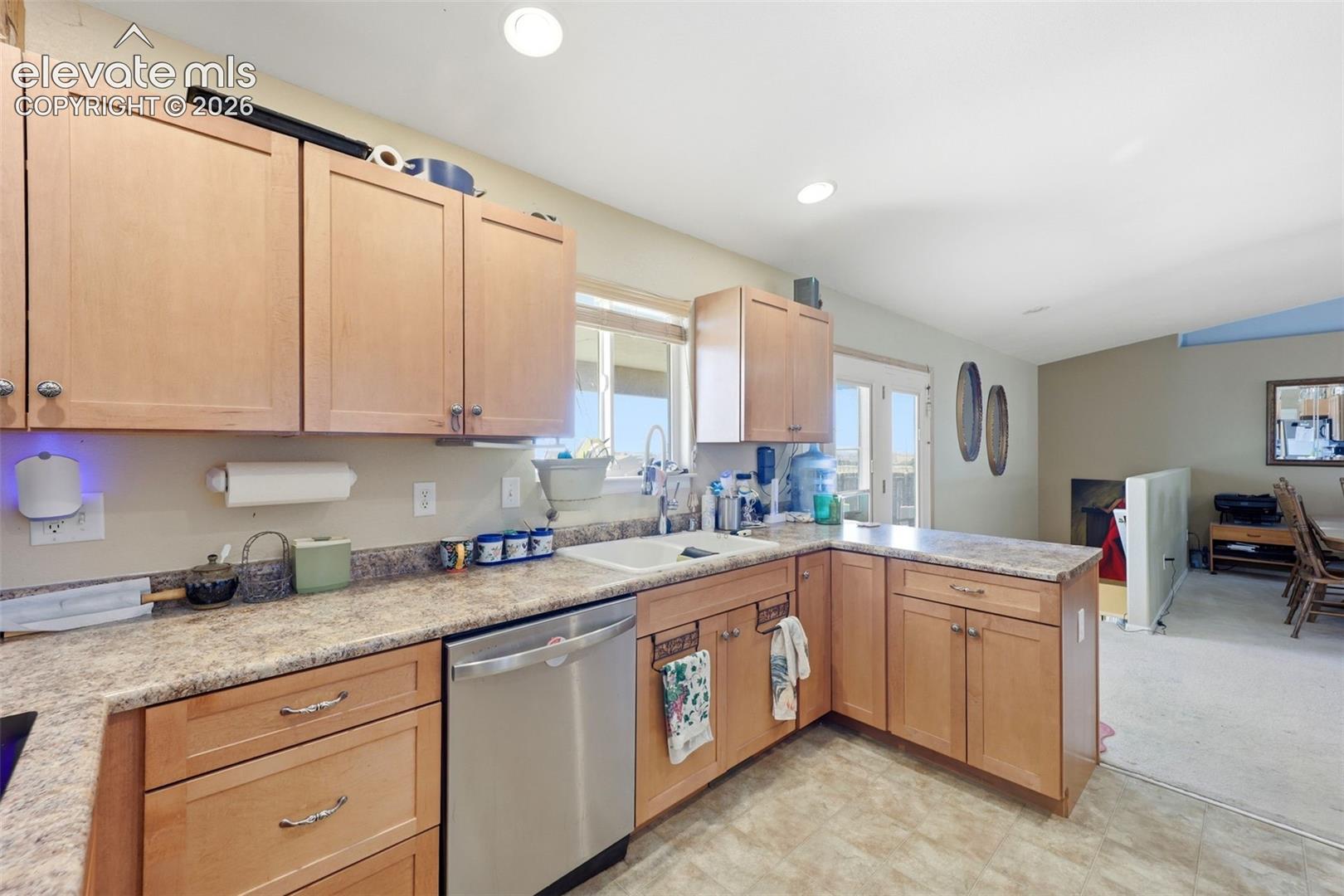 Kitchen featuring light wood cabinetry, a stainless steel dishwasher, a single basin sink, and laminate countertops