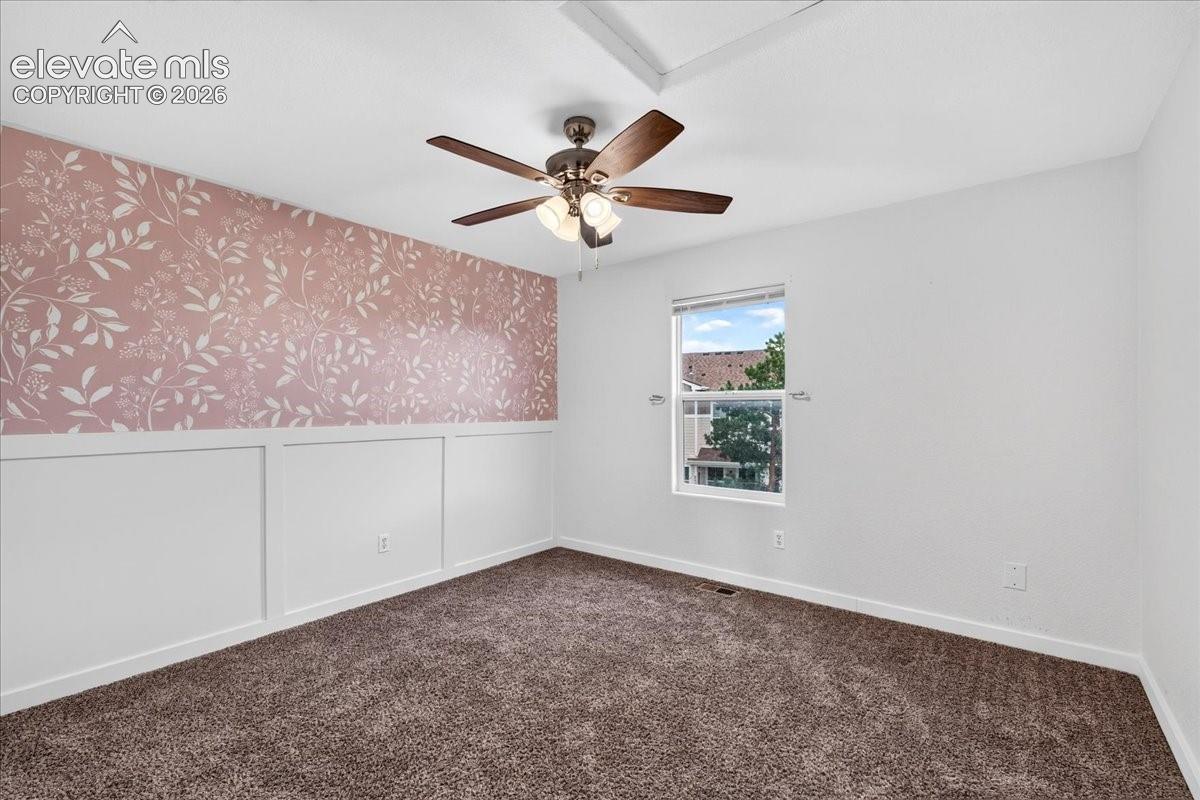 Wall paneling with a patterned accent wall, ceiling fan, and carpeted flooring