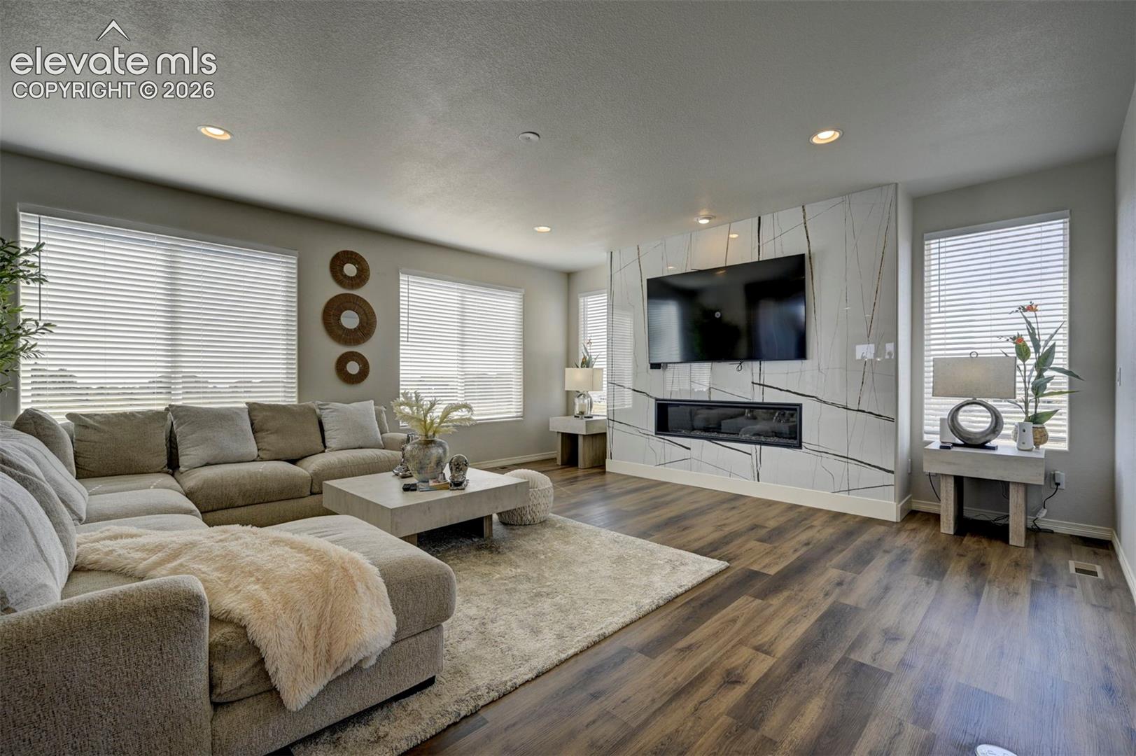 Spacious living area featuring wood-finish flooring, recessed lighting, and multiple windows with blinds