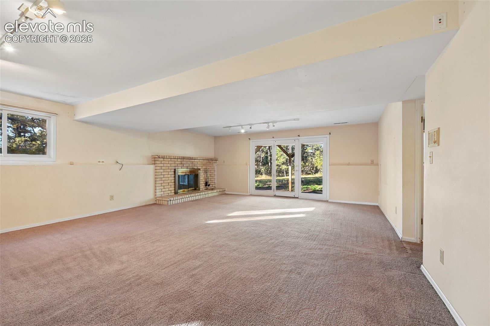 Spacious lower-level room featuring a brick fireplace, carpeted flooring, track lighting, and a glass sliding door