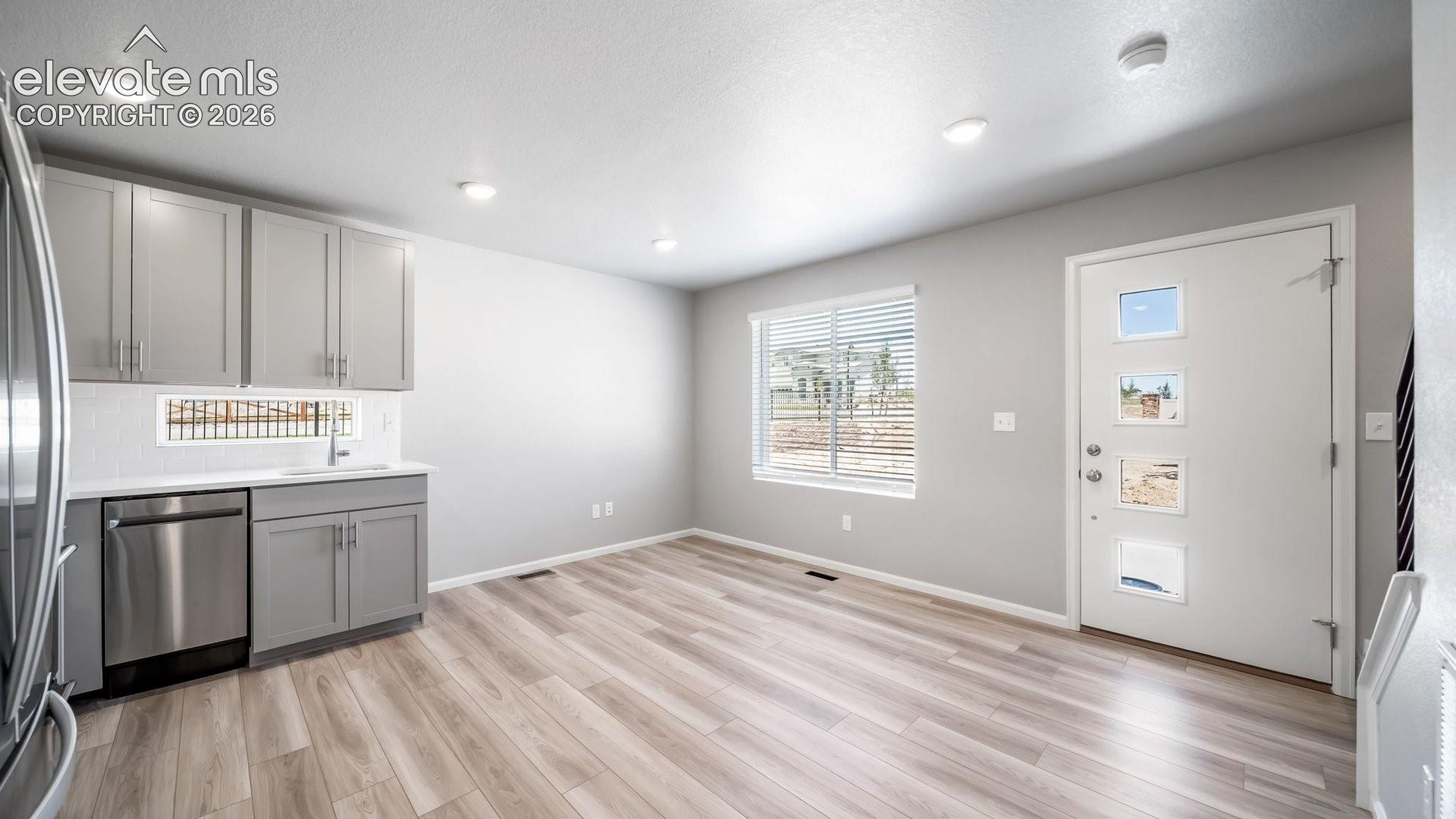 Light-toned wood-finish flooring, shaker-style cabinetry, stainless steel dishwasher, integrated sink, and an exterior door featuring four inset glass panels
*photos of a model home*