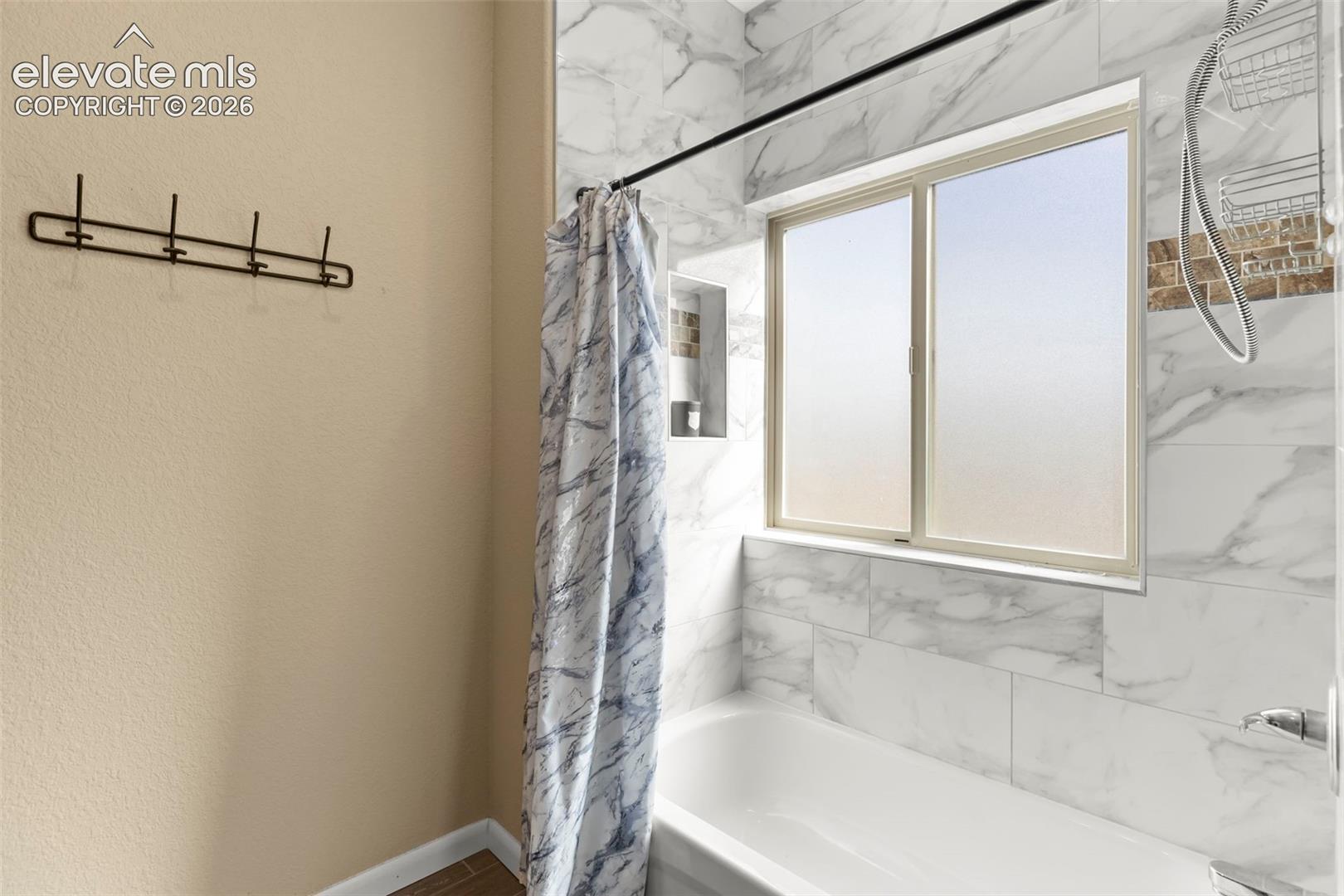 Bathtub featuring large-format wall tiling, a built-in recessed storage niche, and a slider window
