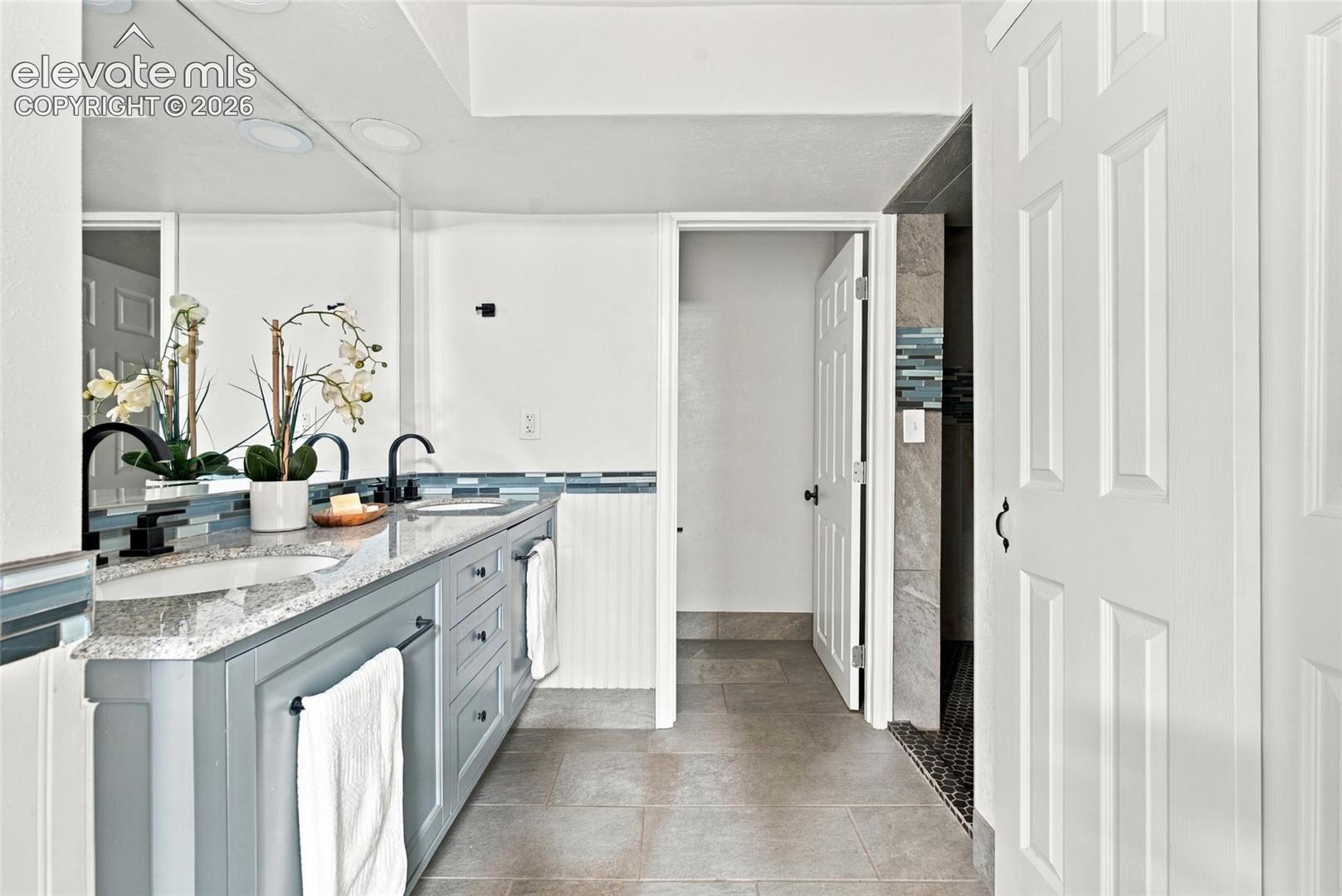 Dual sink vanity with stone countertop, matte black fixtures, and full-wall mirror