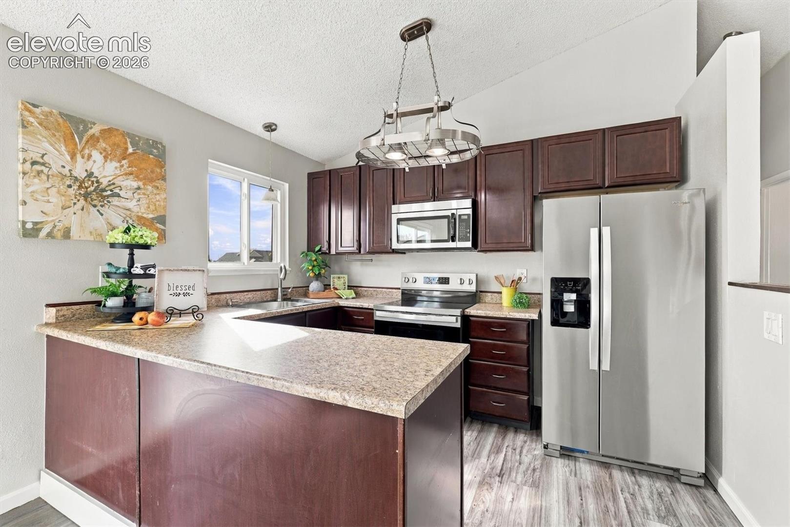 Kitchen featuring dark wood cabinetry, stainless steel appliances, neutral countertops, a peninsula, and vaulted ceilings