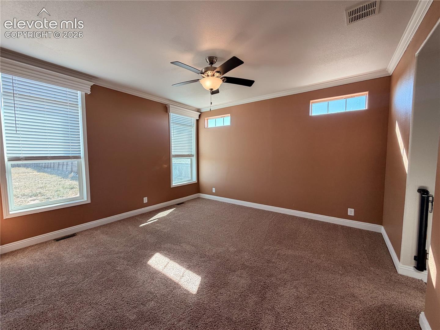 Room featuring wall-to-wall carpeting, crown molding, double-hung windows, horizontal clerestory windows, and a ceiling fan with integrated lighting