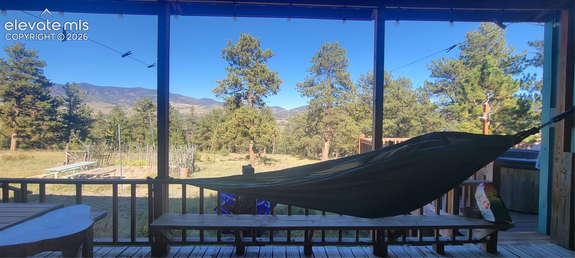 Covered porch with wood-finish decking and railing overlooking a natural landscape with mature trees and distant mountains