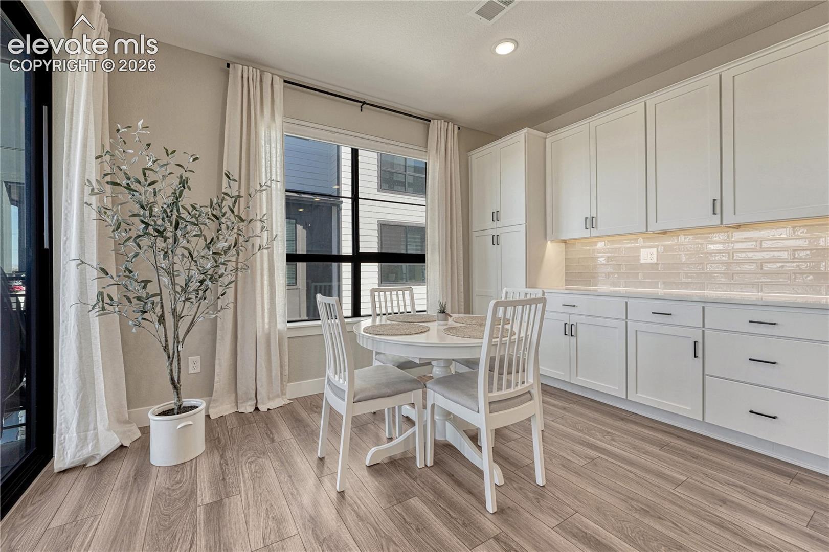 White shaker-style cabinetry, subway tile backsplash, wood-finish flooring, and black-framed windows