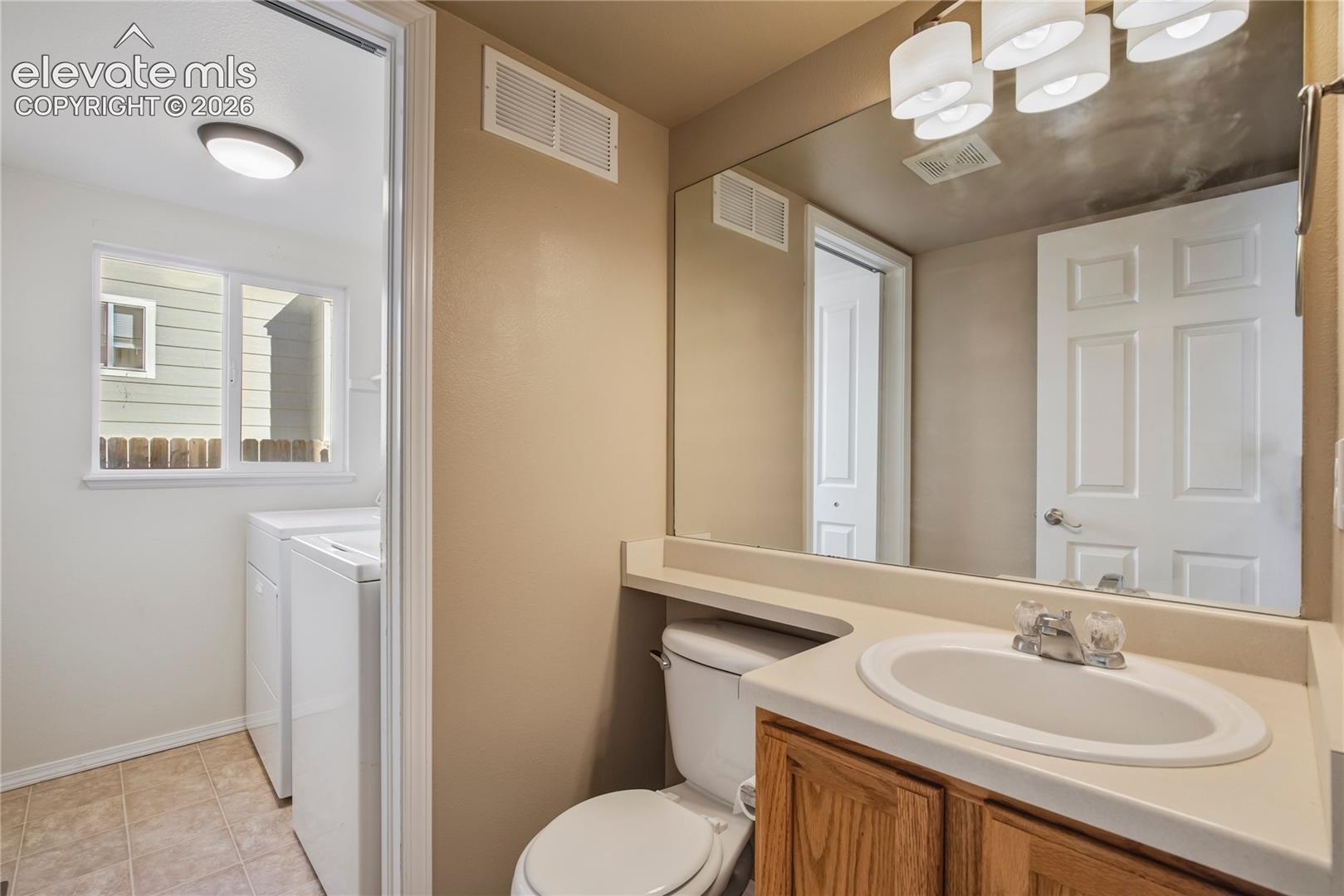 Convenient main-level powder bath features a vanity + mirrored storage, with the nearby laundry area offering electric hookups and a window for natural light.