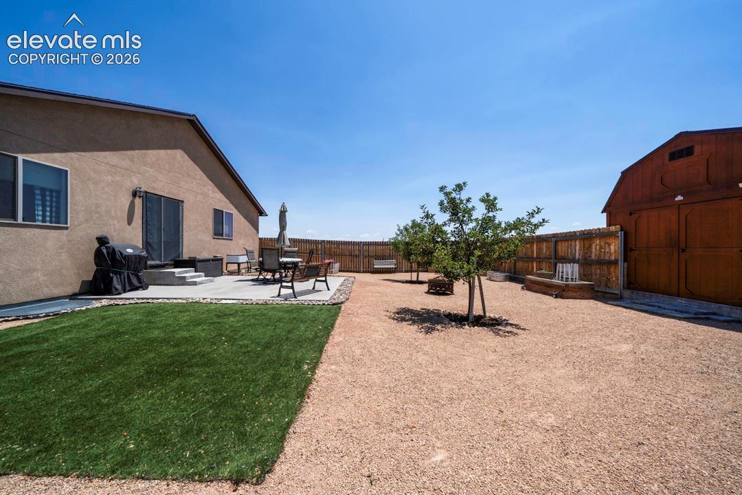 Expansive backyard featuring a stucco exterior, a concrete patio, a privacy fence, a detached barn, and a combination of artificial turf and gravel landscaping