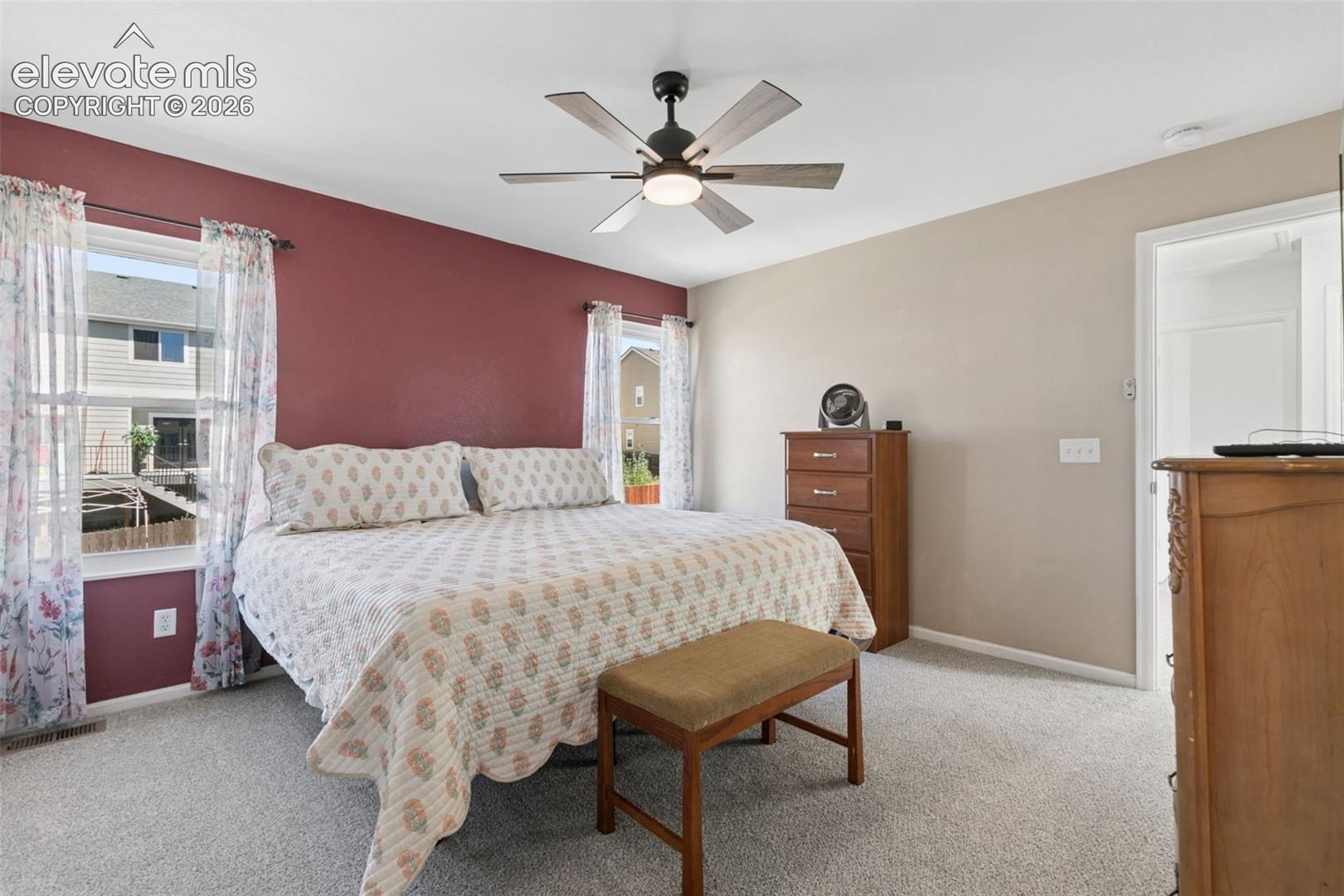Ceiling fan with integrated lighting, dual windows, neutral-toned carpeting, and an interior doorway
