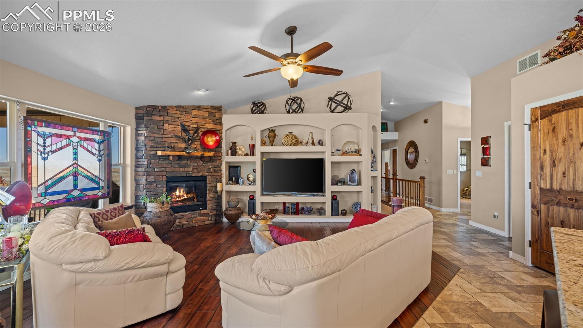 Living room with a ceiling fan, plenty of natural light, a fireplace, stone finish floors, and lofted ceiling