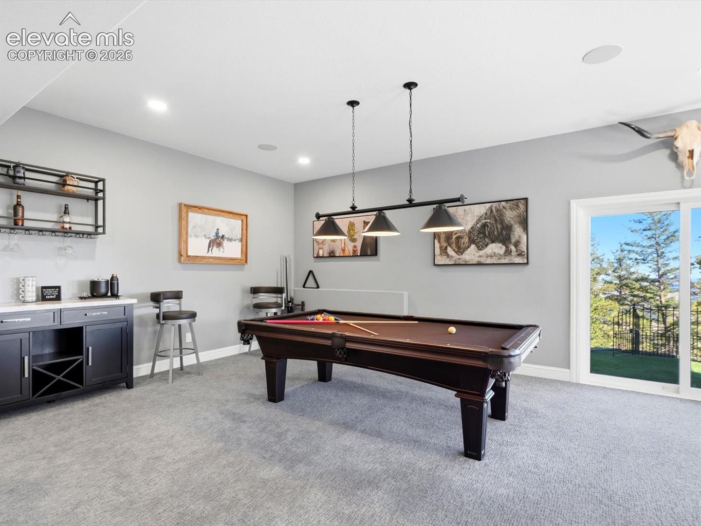 Built-in dark cabinetry featuring wine storage and a countertop, recessed lighting, triple-pendant light fixture, and glass sliding door