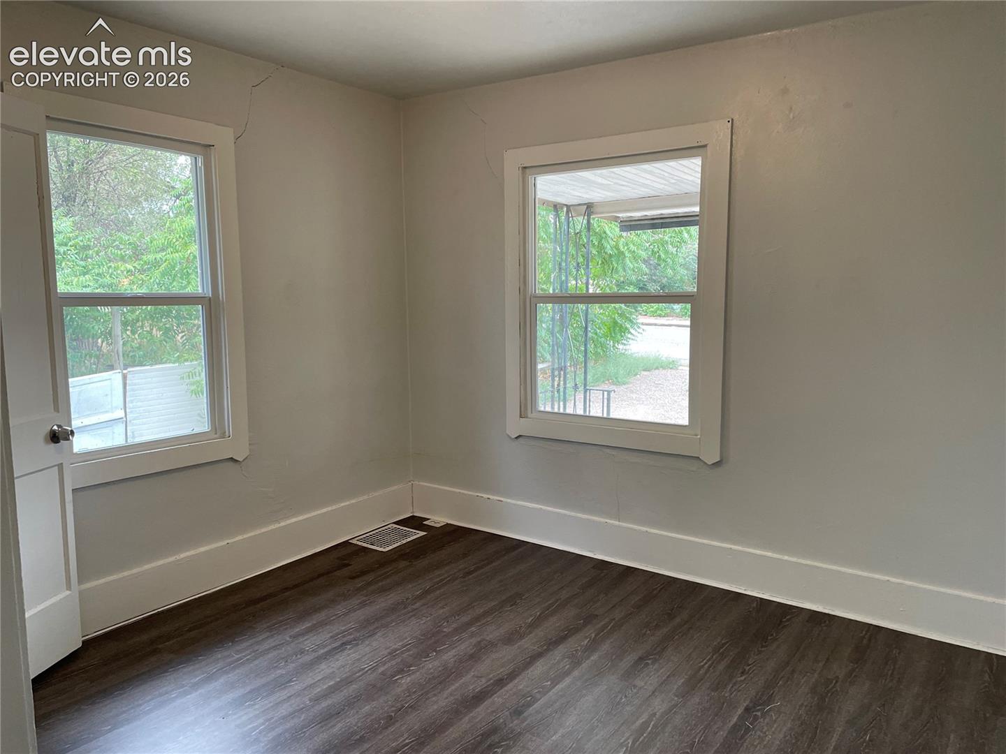 Room with dark wood-finish flooring and two windows with white trim