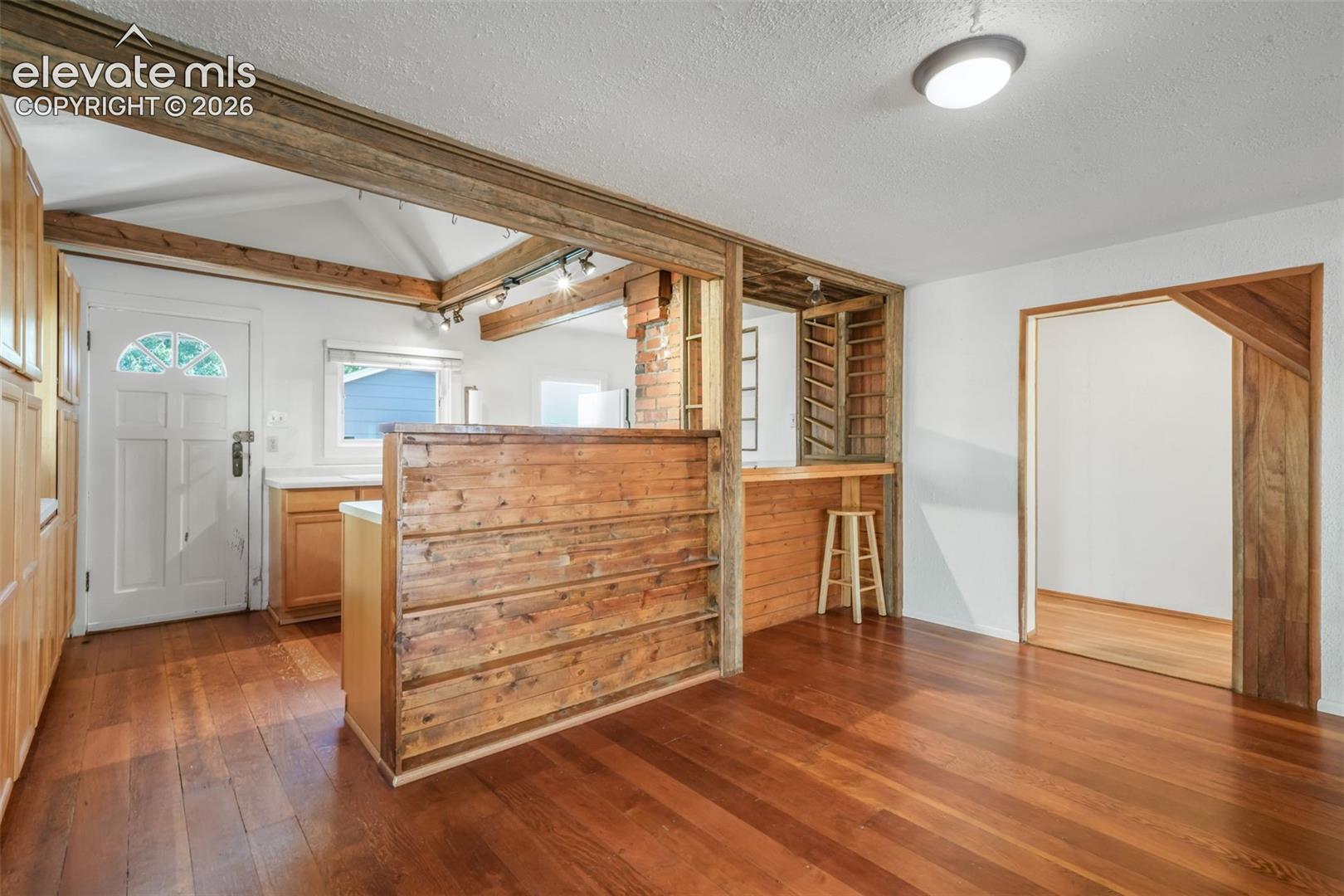 Hardwood flooring, wood-clad architectural features, white walls, built-in shelving, and a wood-paneled bar