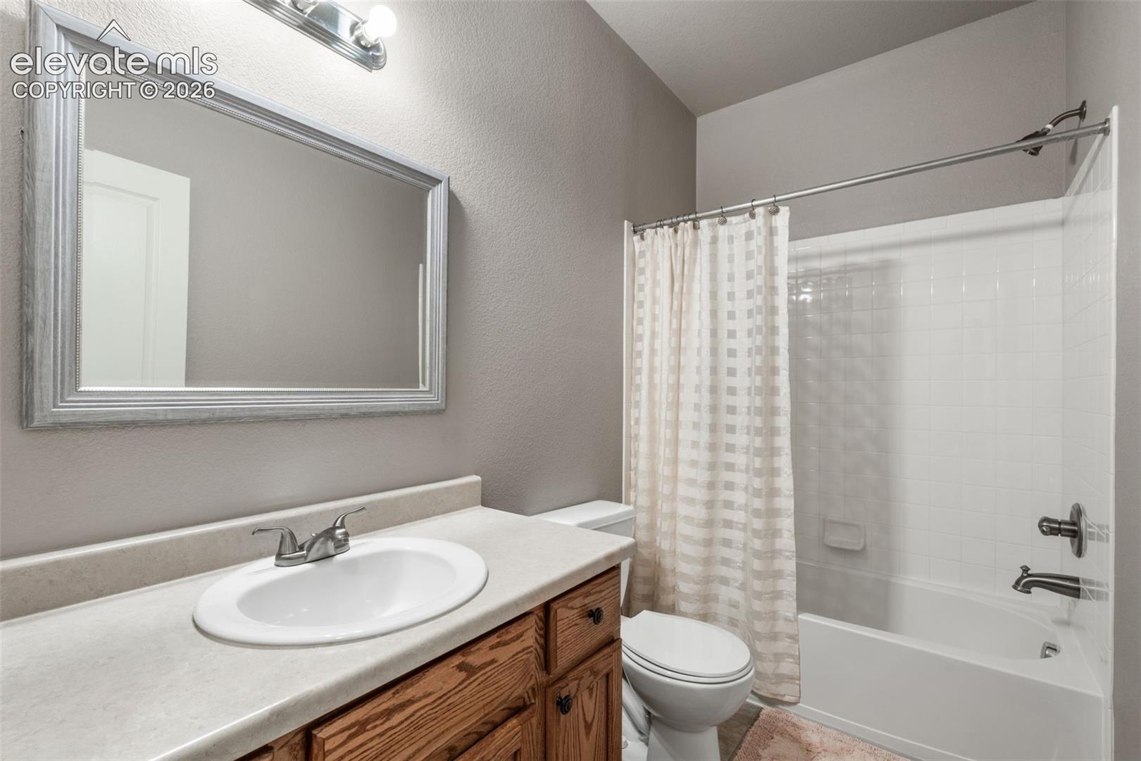 Bathroom featuring a wood vanity with a solid-surface countertop, integrated basin, framed wall mirror, and a tub-shower combination with white wall tile