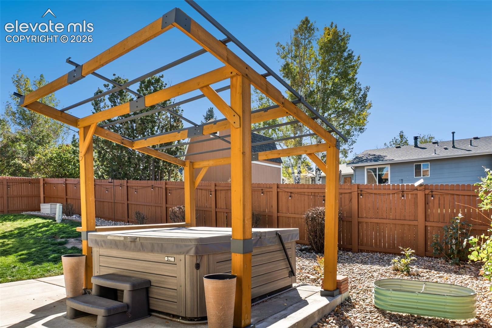 Backyard outdoor space featuring a timber-frame pergola, built-in hot tub, concrete patio, and fenced perimeter